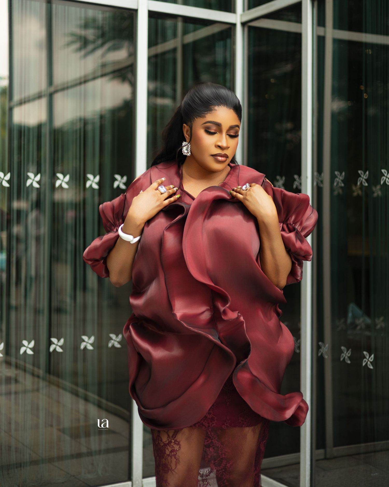 Dramatic outdoor portrait with burgundy ruffled statement dress against glass building backdrop.