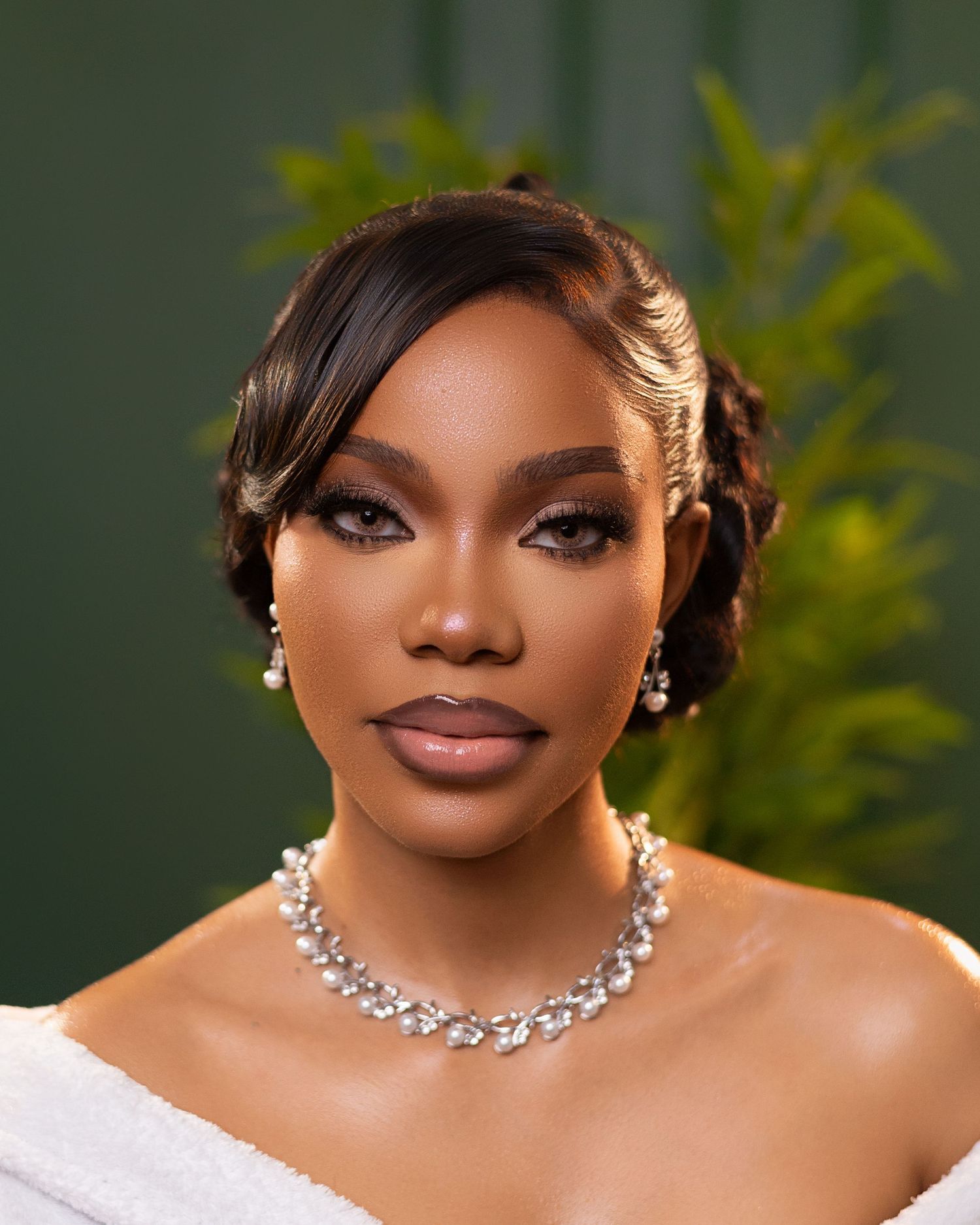 Studio portrait featuring elegant jewelry and white off-shoulder dress against a green background.