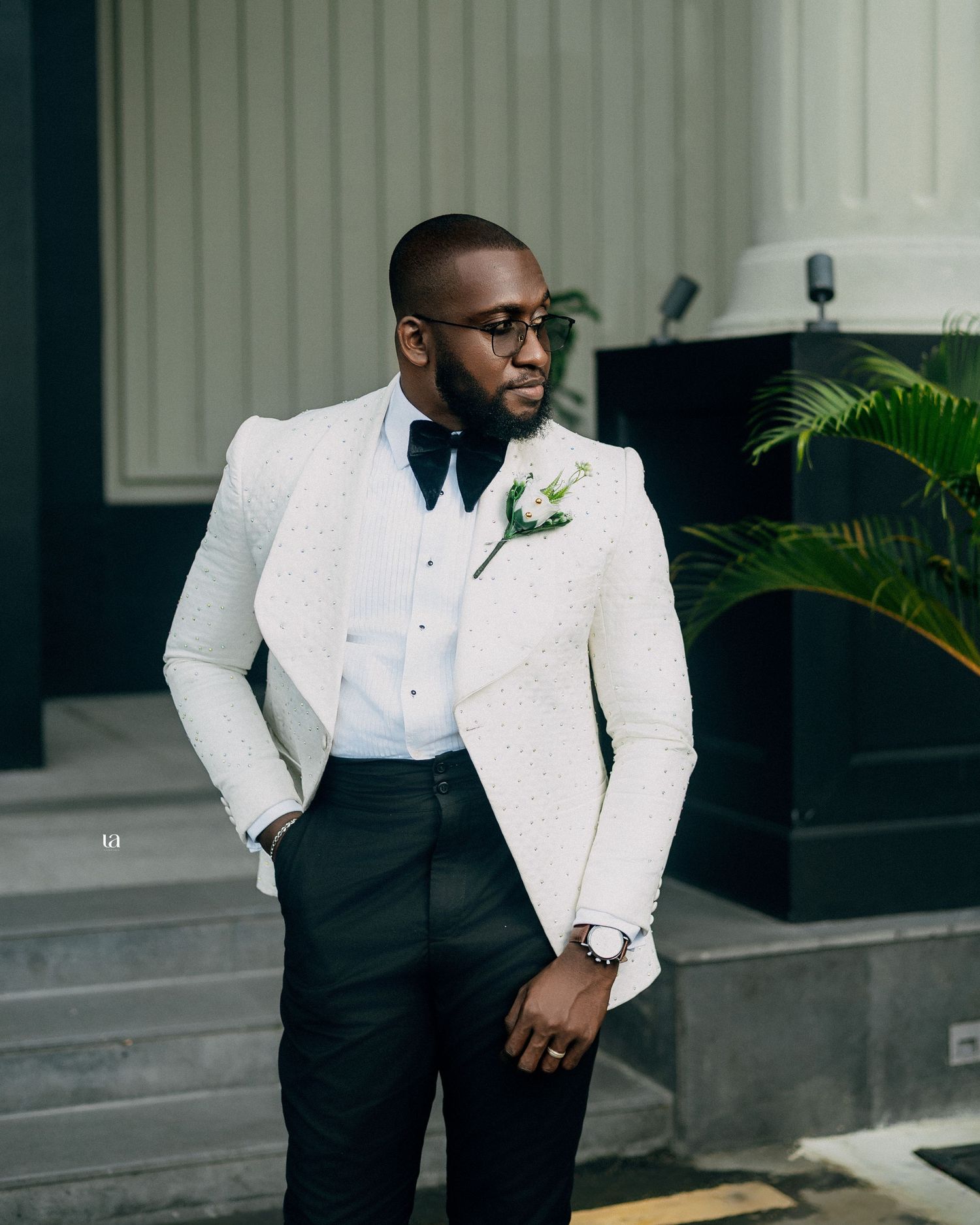 Elegant wedding fashion featuring a white tuxedo jacket paired with black trousers in an outdoor setting.