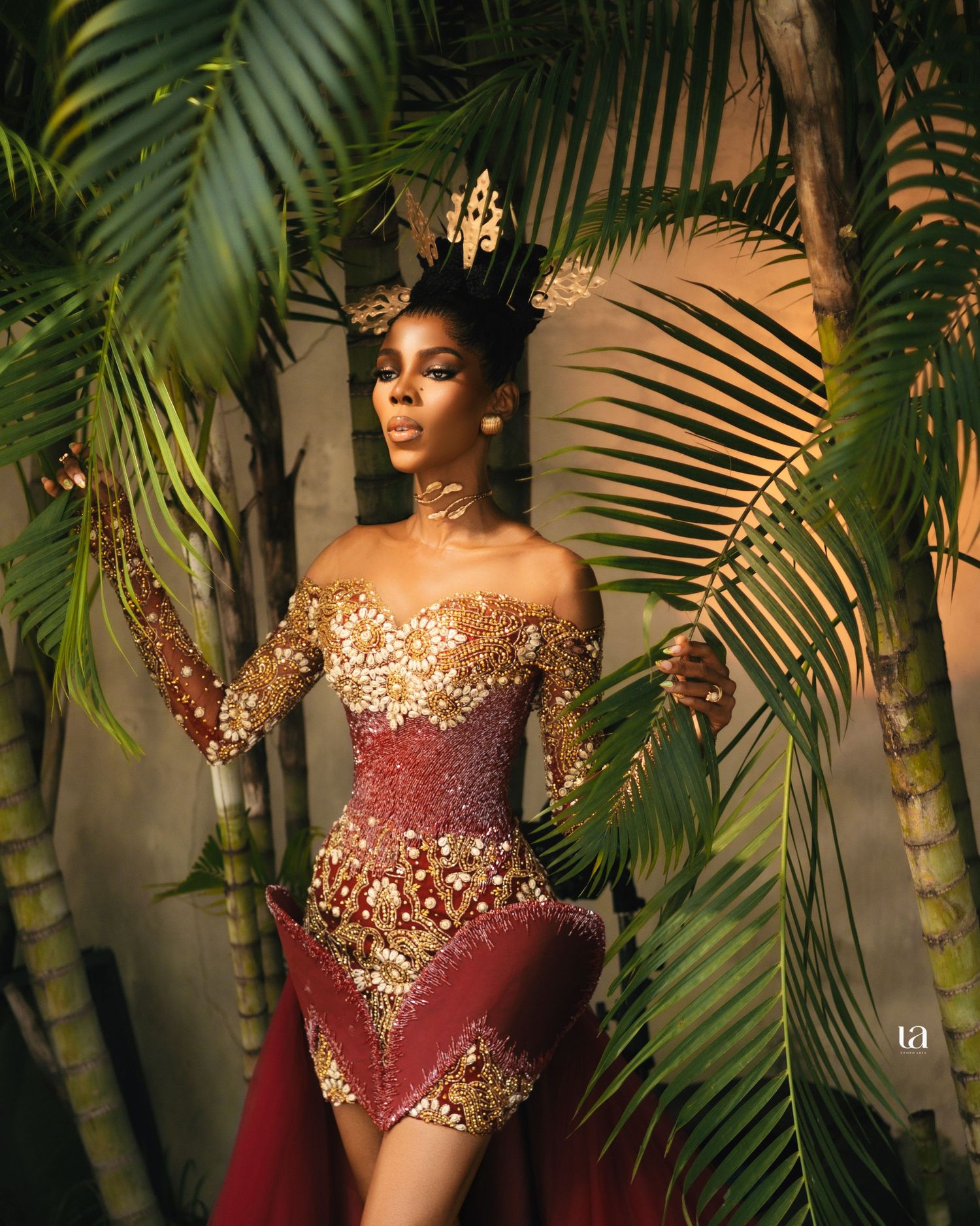 Luxury burgundy and gold gown photographed against tropical palm trees.