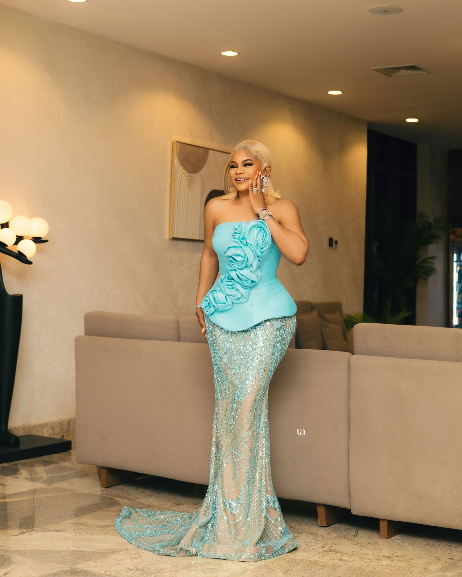 Elegant poses in a turquoise sequined gown against a neutral indoor setting.