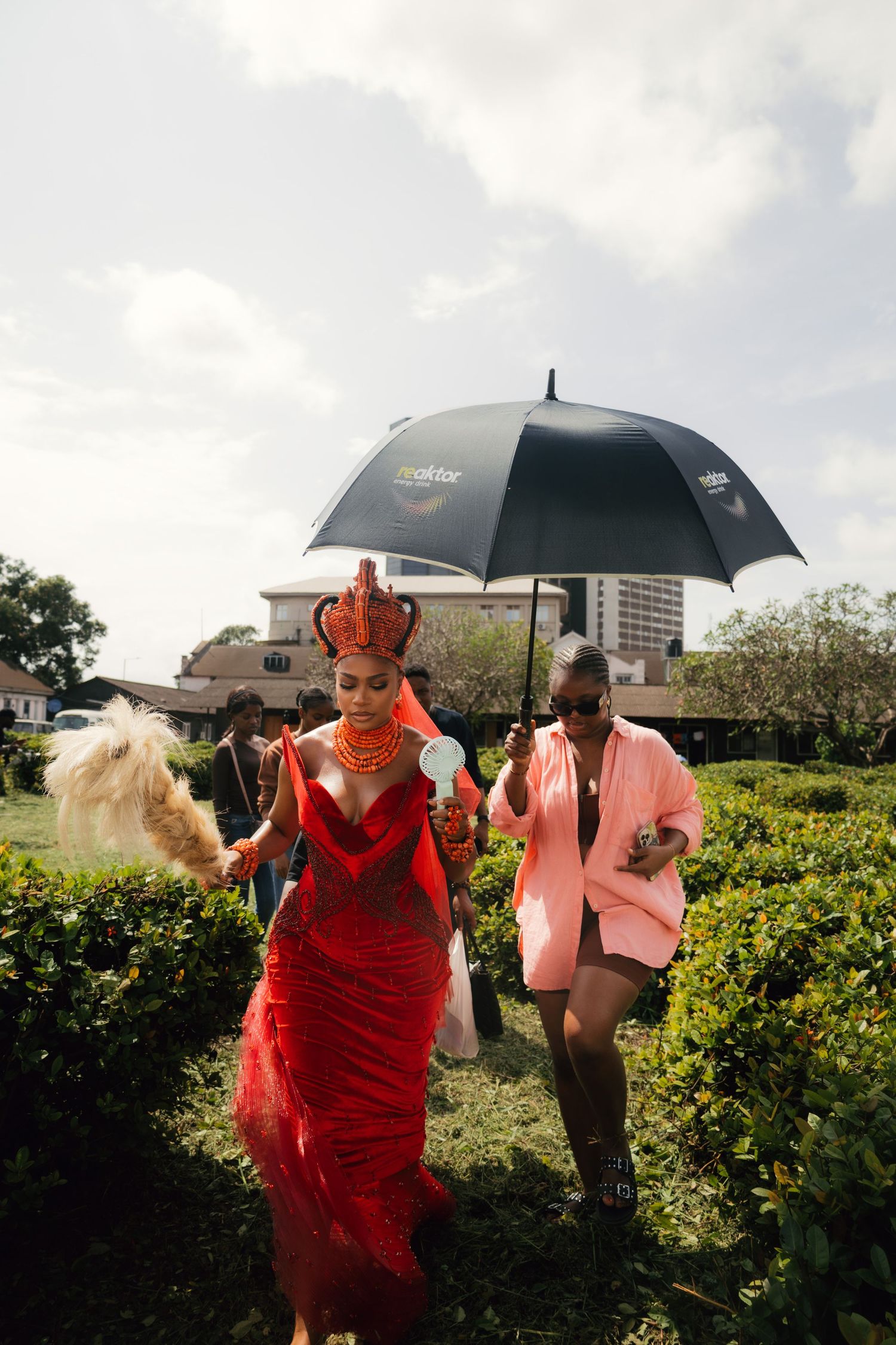 Wedding party members with black umbrellas walk through garden landscape.