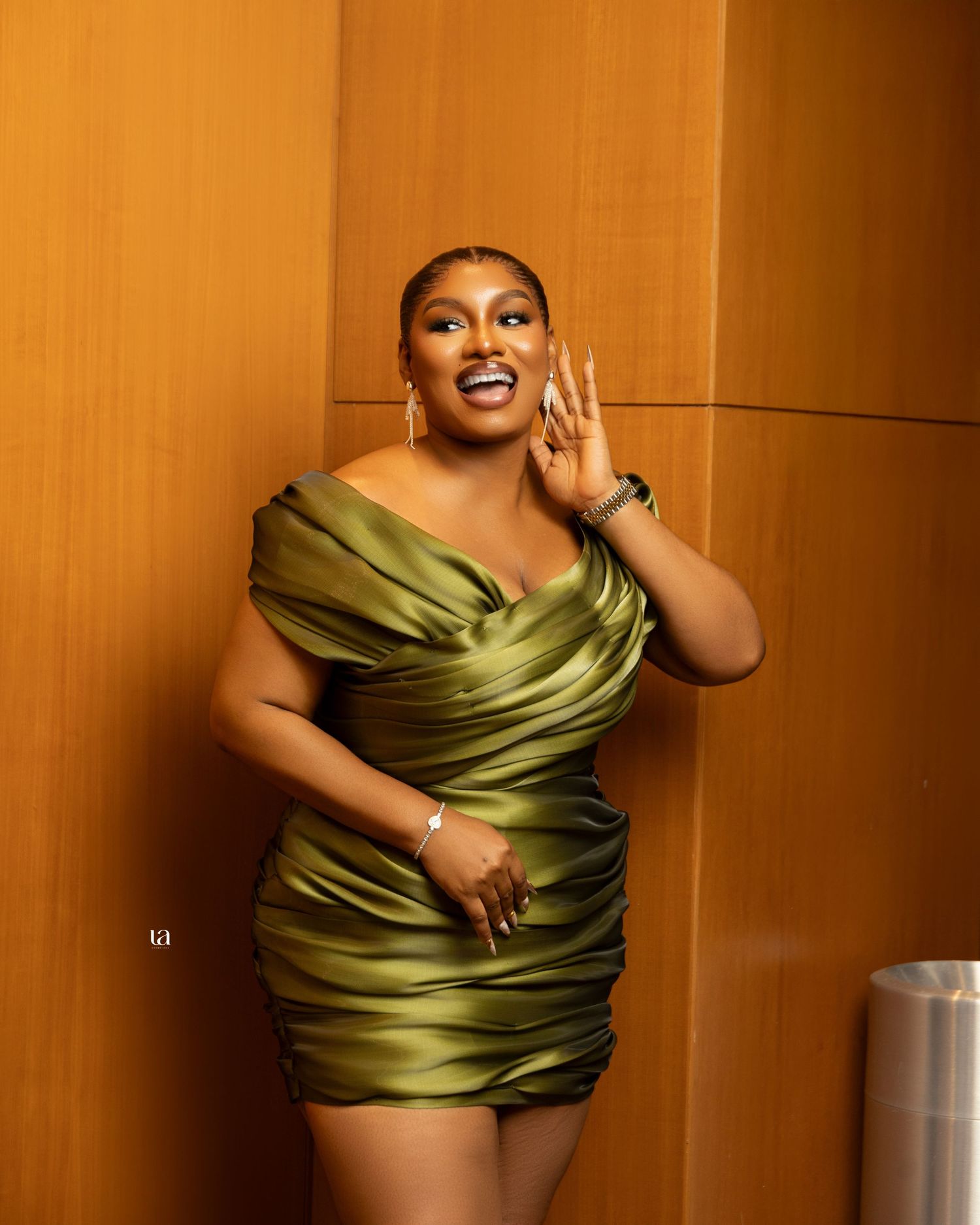 Fashion sequence featuring olive green satin wrap dress against warm wood paneled background.