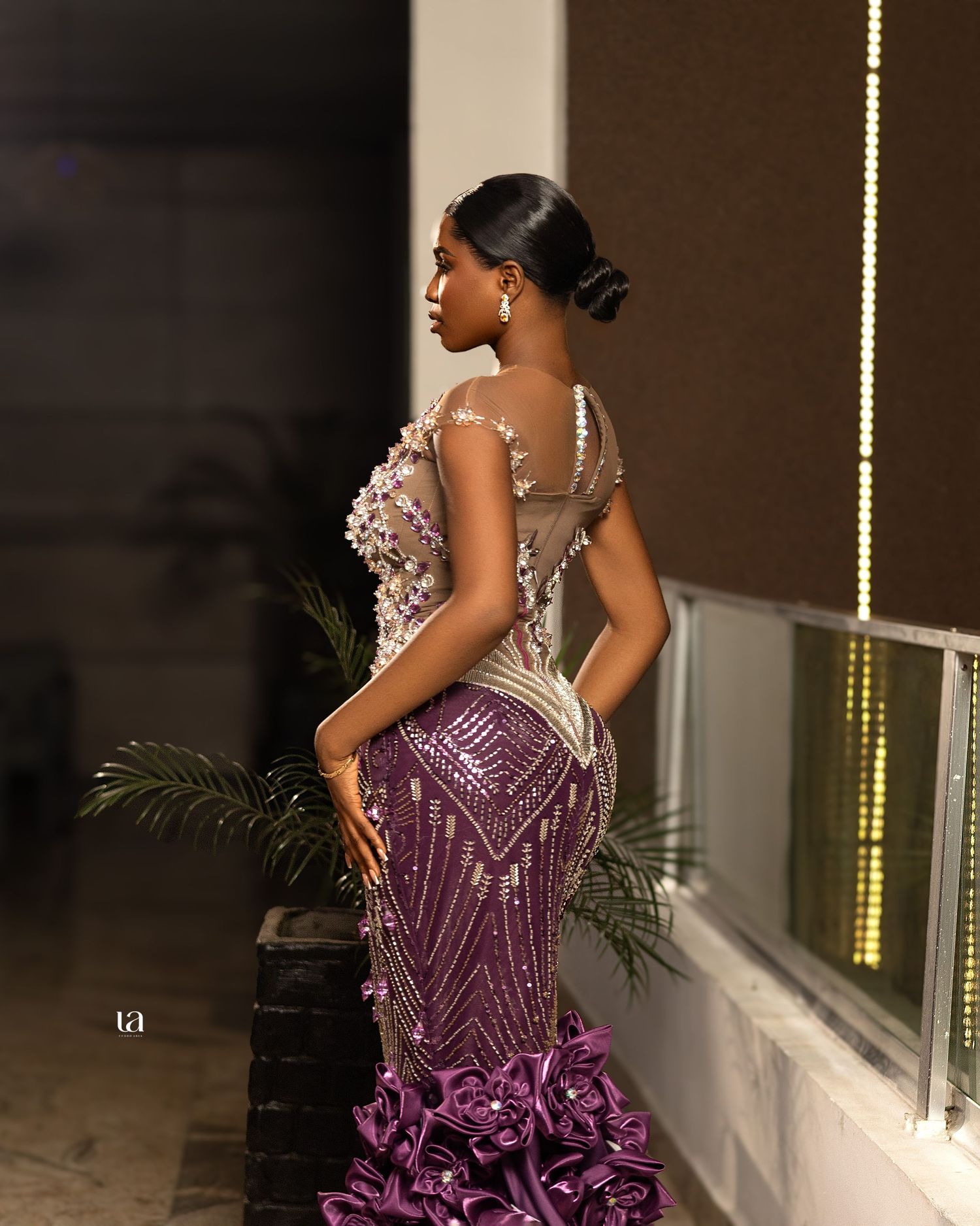 Model strikes elegant pose in purple beaded gown with dramatic ruffled hem.