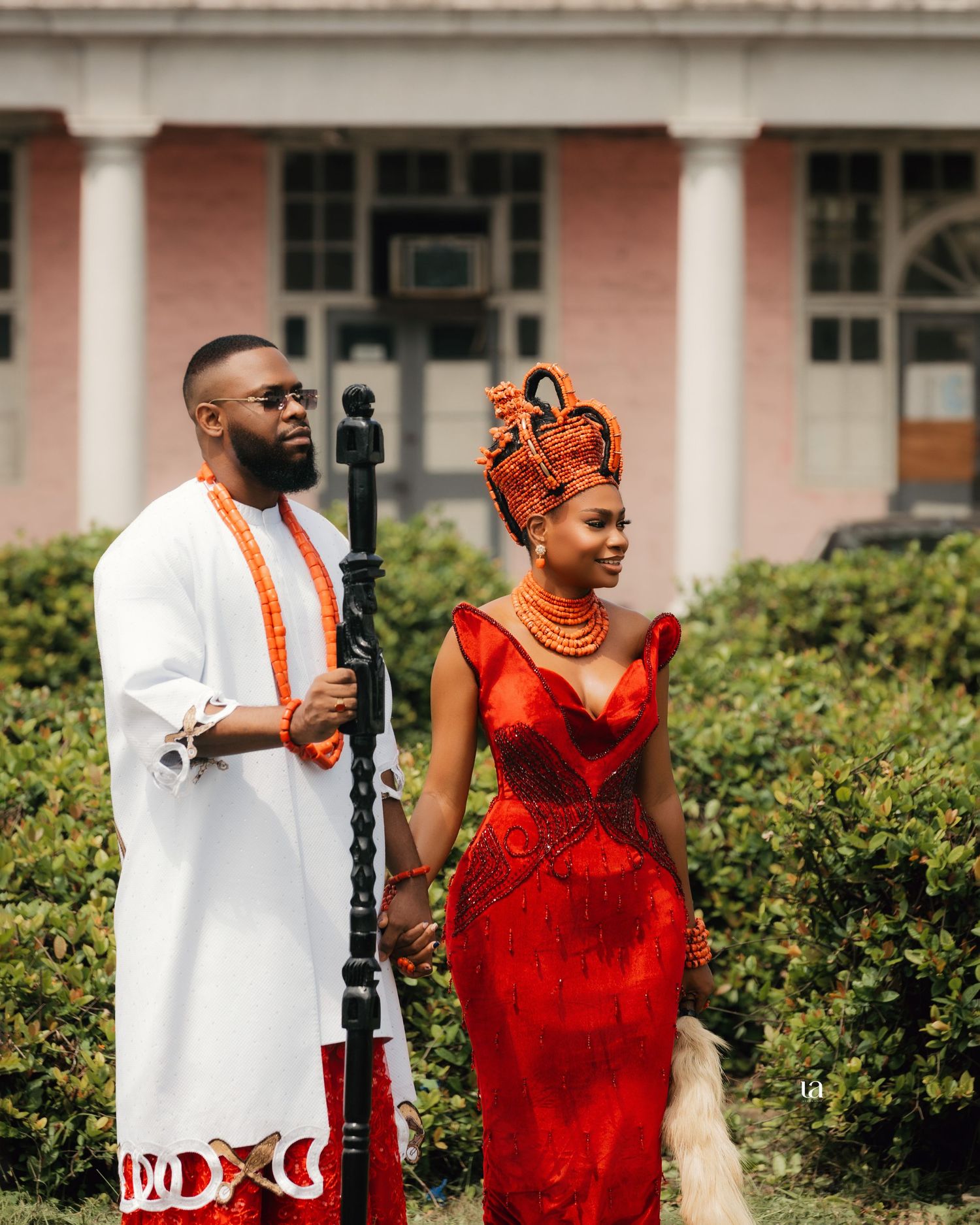 Wedding party in red and white formal attire poses in front of colonial architecture.