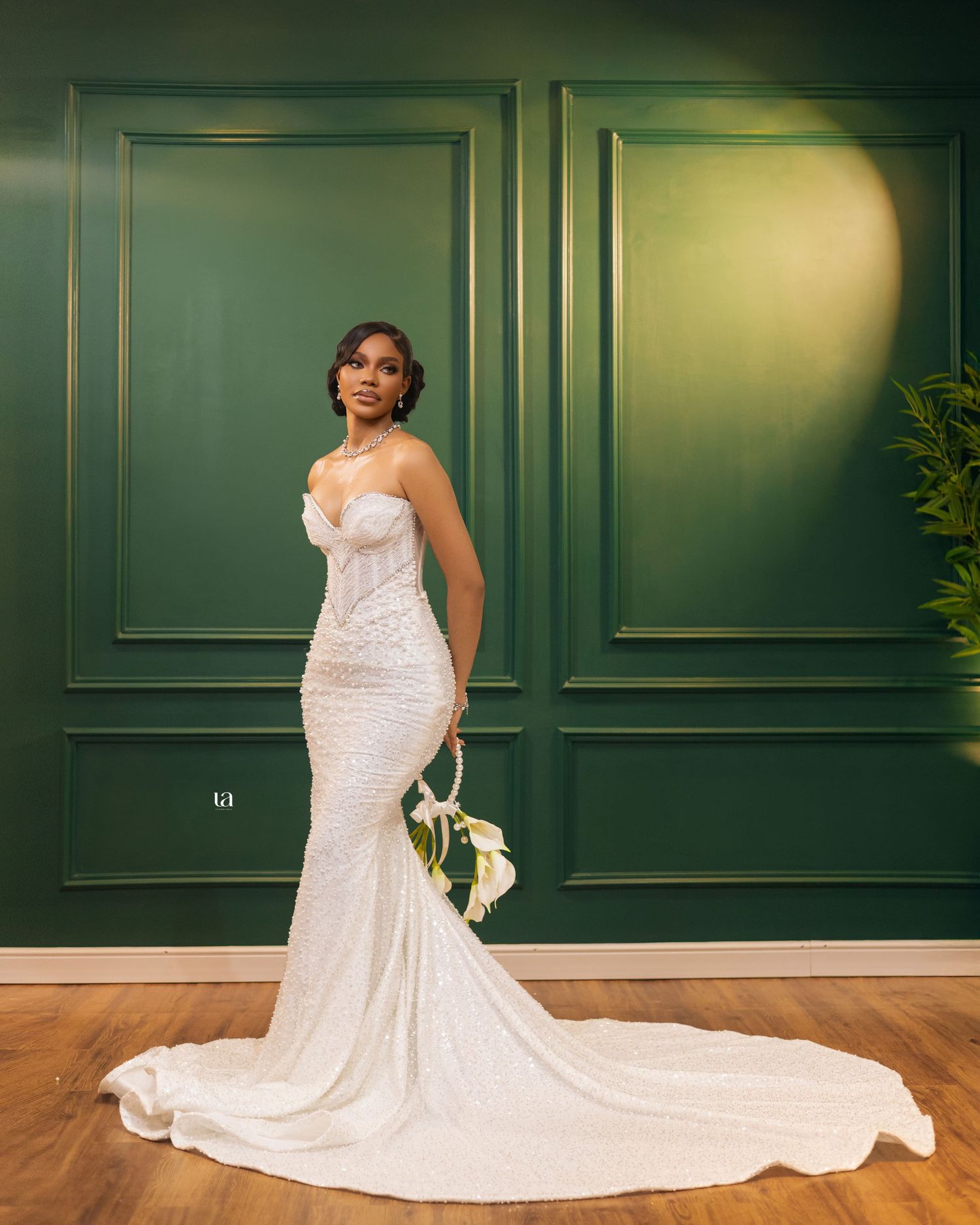 Stunning mermaid wedding gown with intricate beading displayed against an emerald green paneled wall.