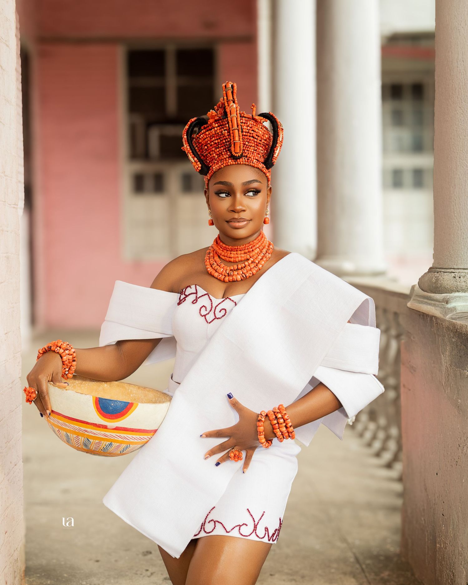 White traditional outfit with orange accessories photographed against colonial architecture.