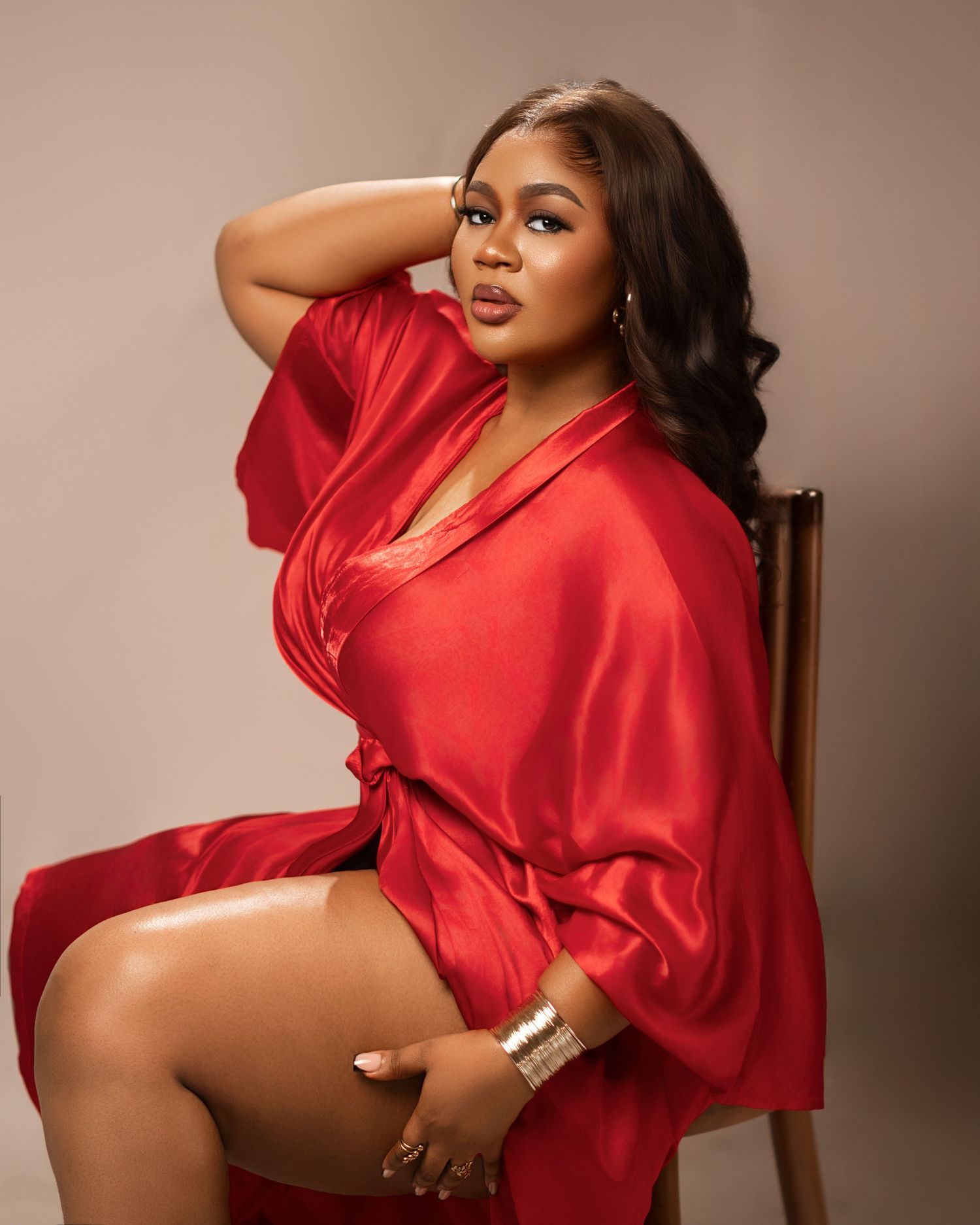 Glamour photoshoot featuring a red silk robe-style dress on a wooden chair.