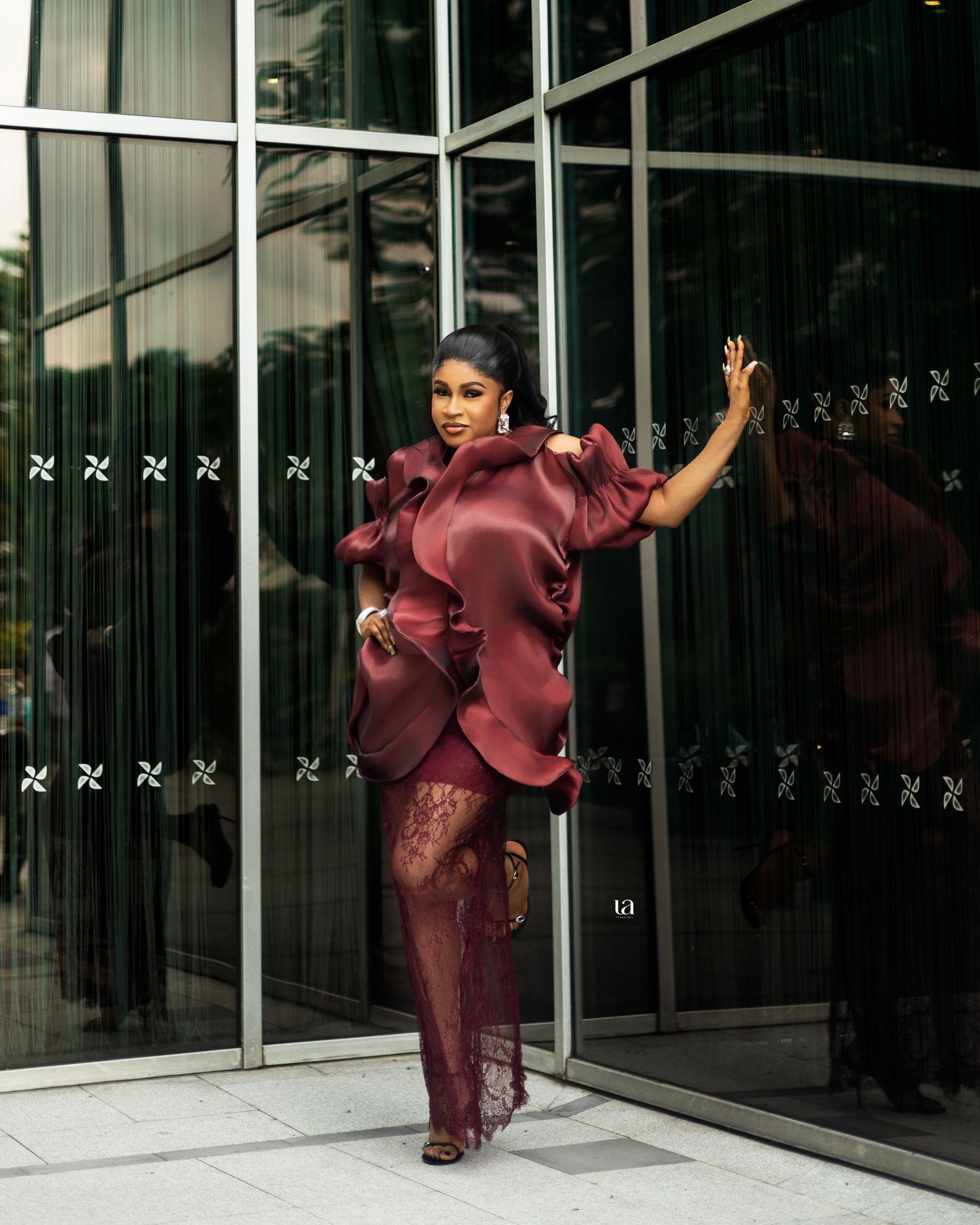 Dynamic fashion shoot in burgundy silk outfit against modern glass building exterior.