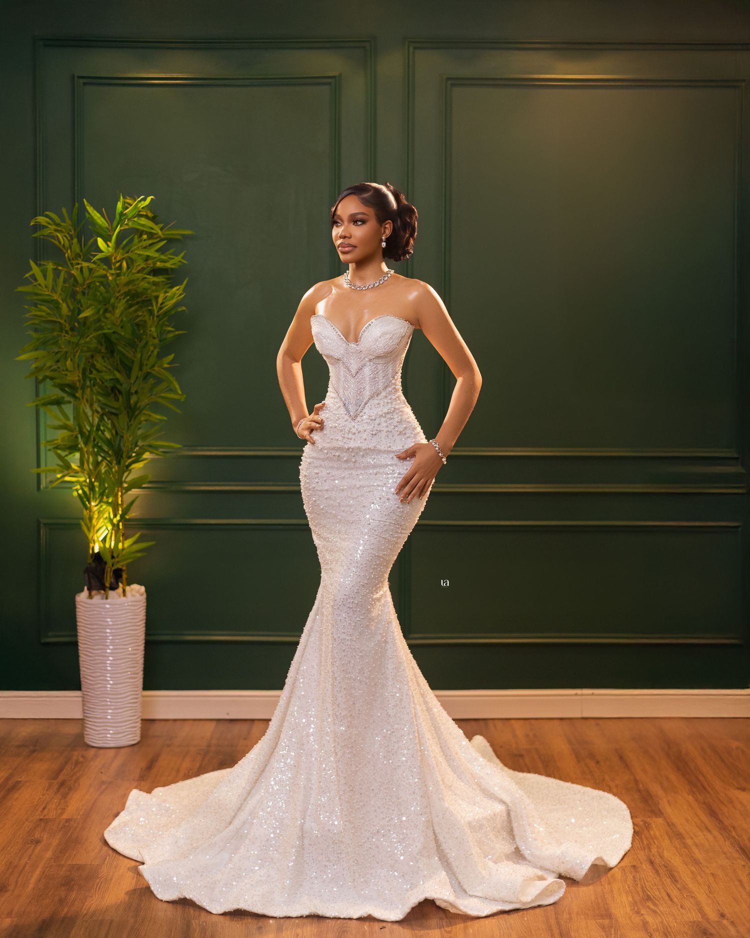 Sparkling fitted wedding dress with dramatic train showcased against dark green wall panels.