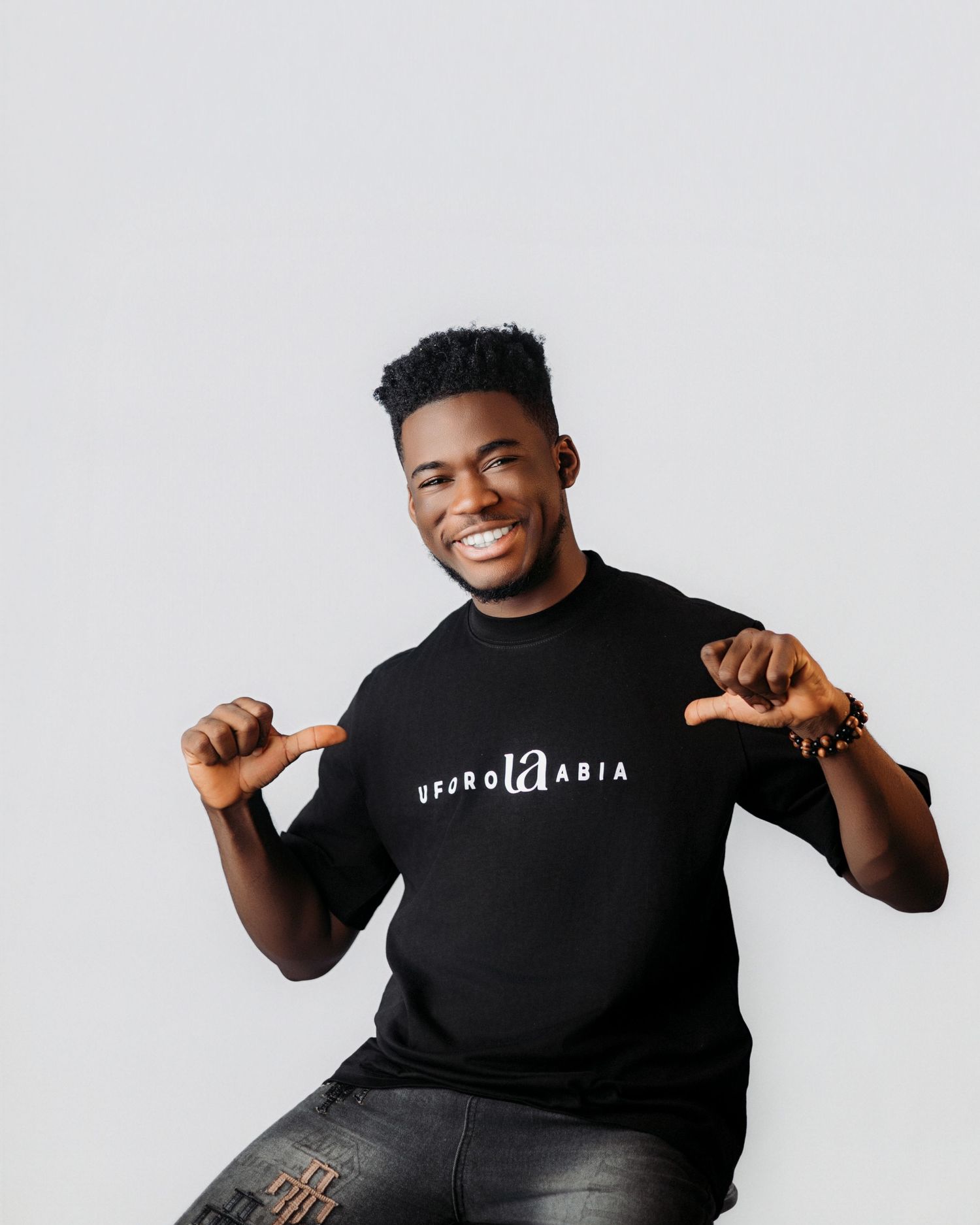 Joyful portrait of person pointing to logo on black t-shirt against white background.