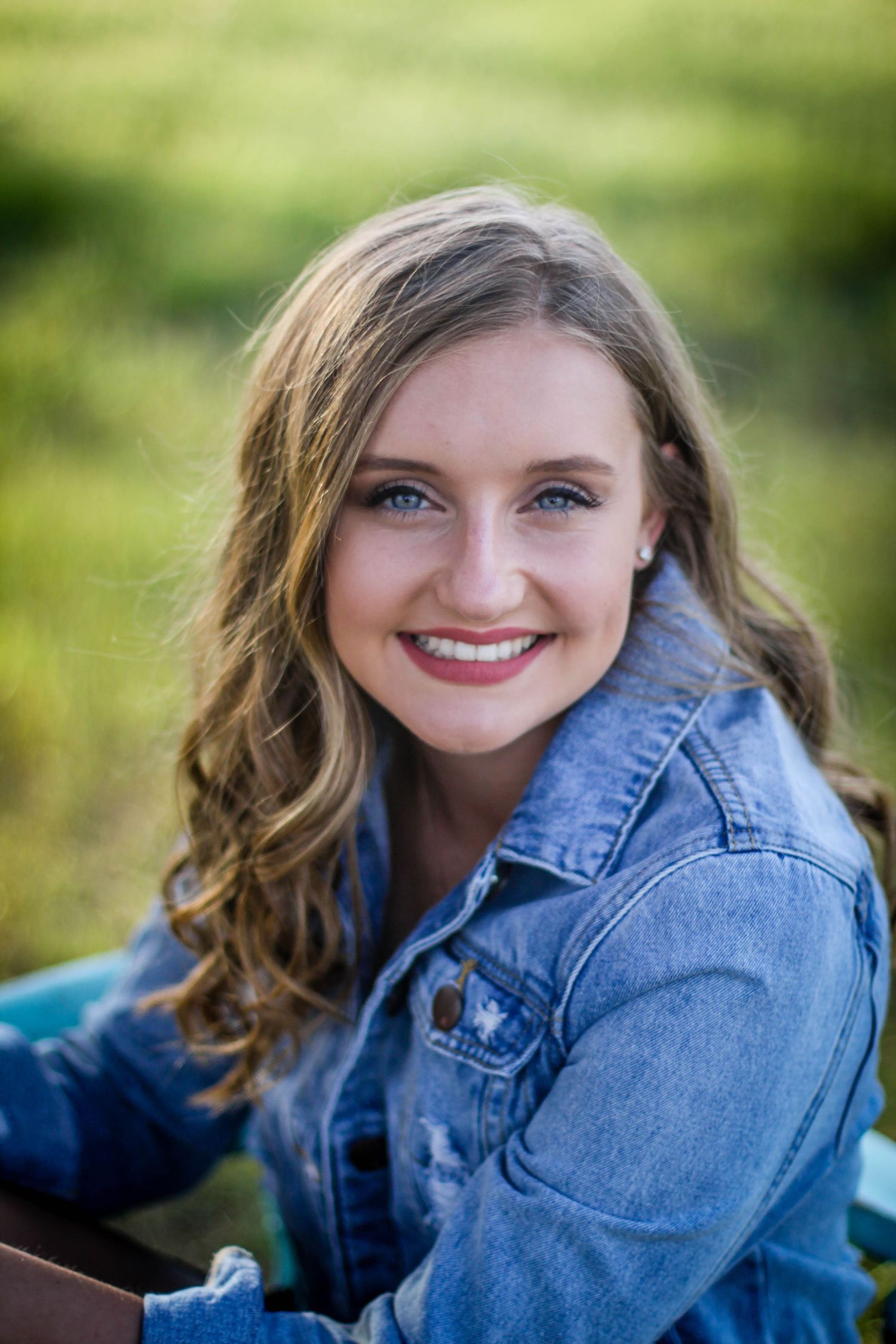 Senior Portrait session in denim jacket against blurred natural background.