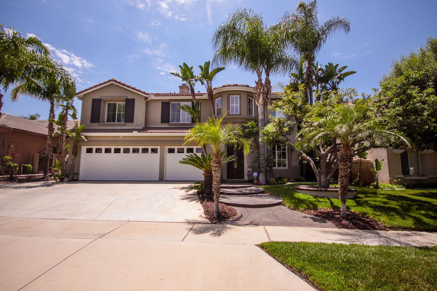 Luxurious Mediterranean-style home exterior with palm trees and circular driveway.