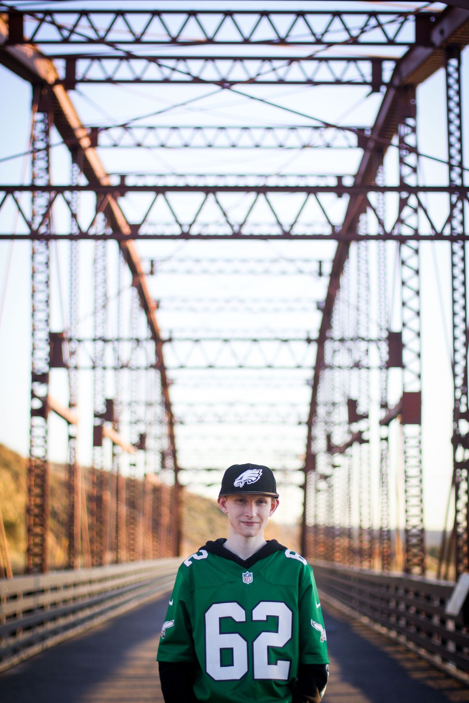 Sports fan poses on metal bridge wearing green jersey number 82.