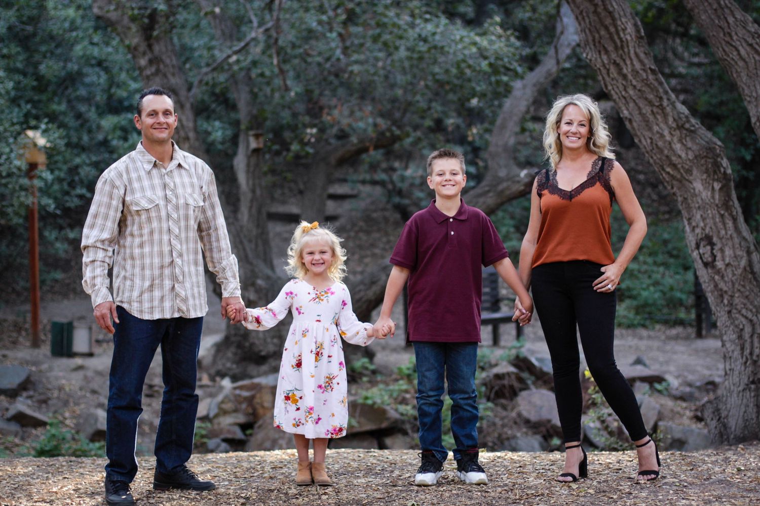 A family walks together outdoors in a natural setting with pine trees and rocks in the background.