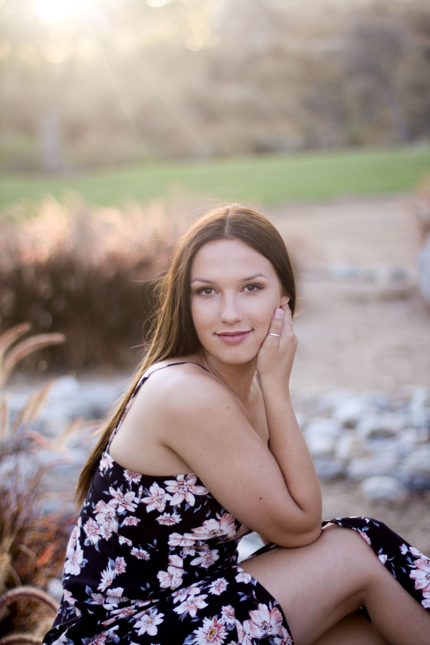 Woman in floral dress poses outdoors during golden hour photography session.