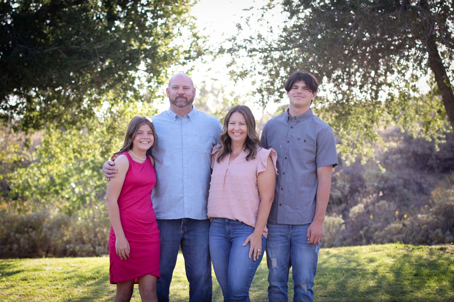 Family members pose together in casual attire against a natural outdoor backdrop.