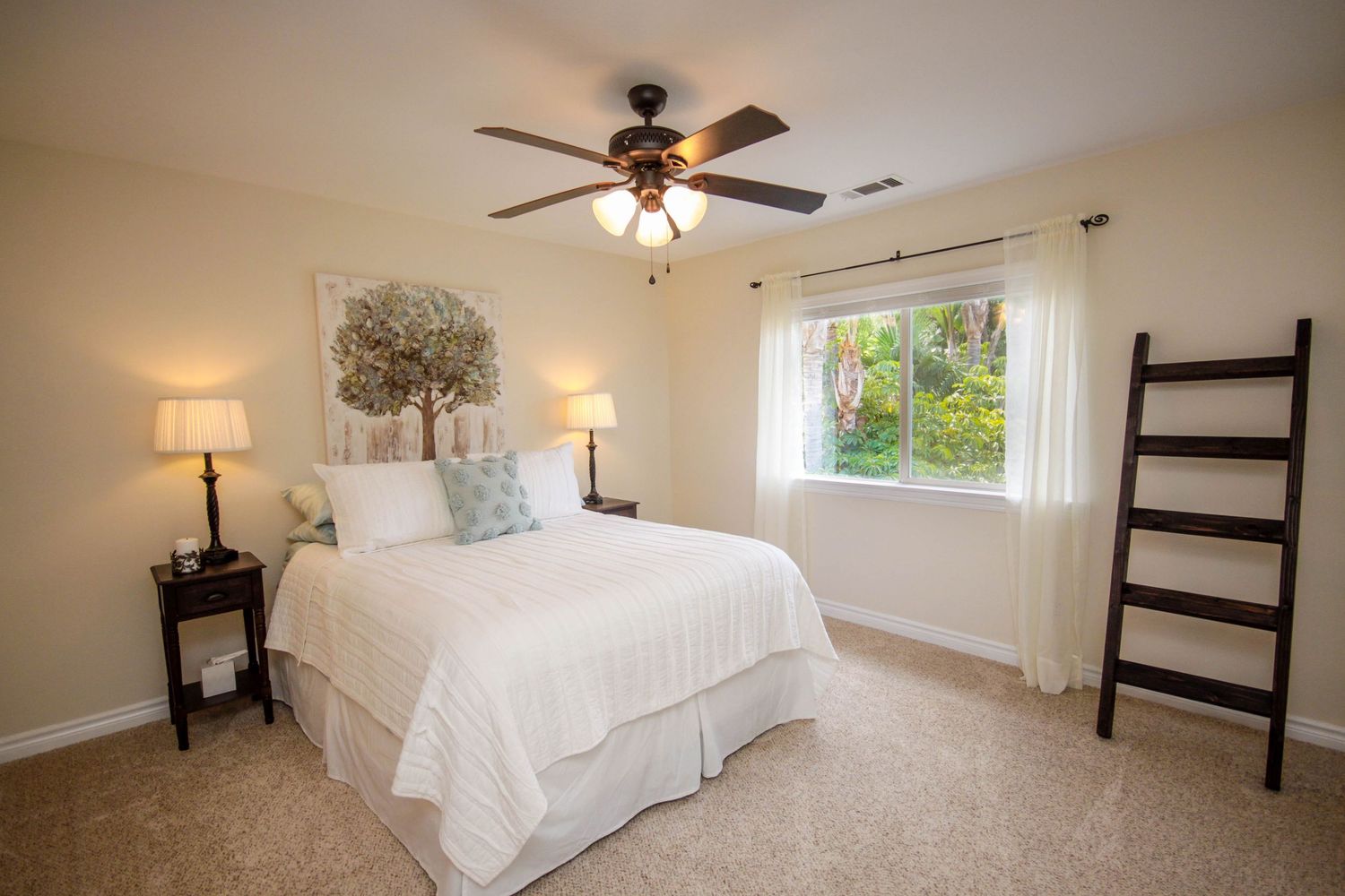Spacious bedroom with ceiling fan, white bedding, and natural light from windows.