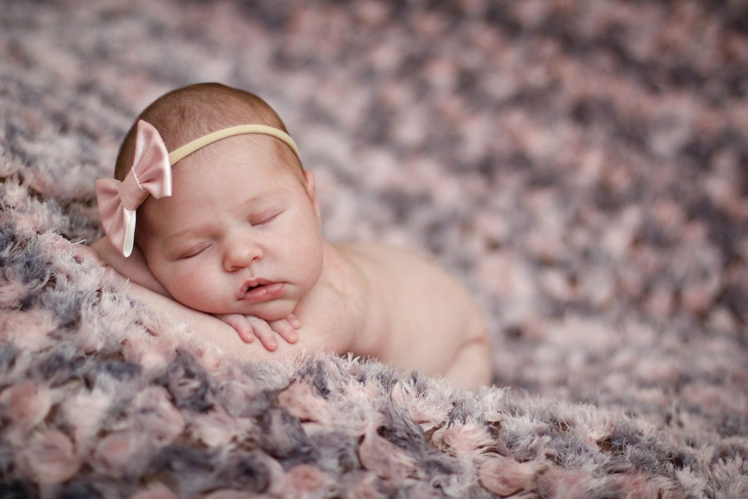 Newborn baby sleeping on soft brown textured blanket with delicate headband.