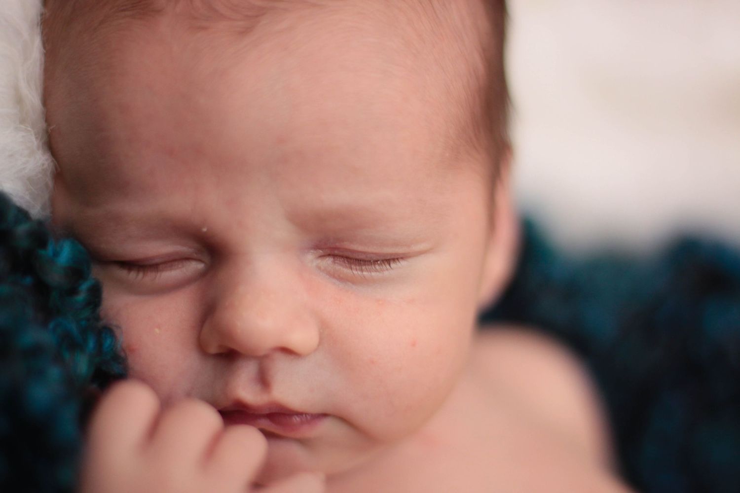 Peaceful sleeping newborn with green headband against dark background.