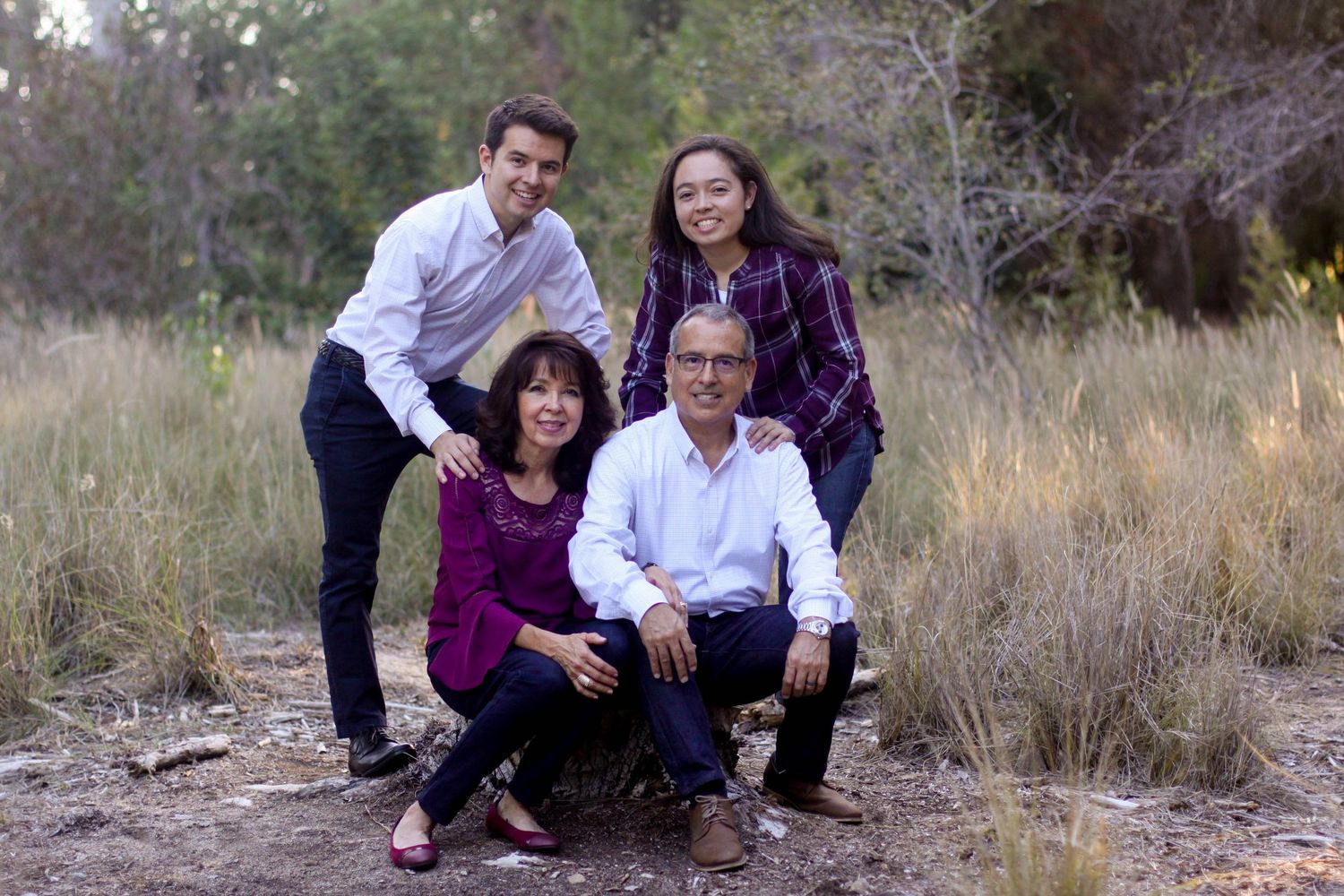 A family poses together in a natural outdoor setting with tall grass and trees.