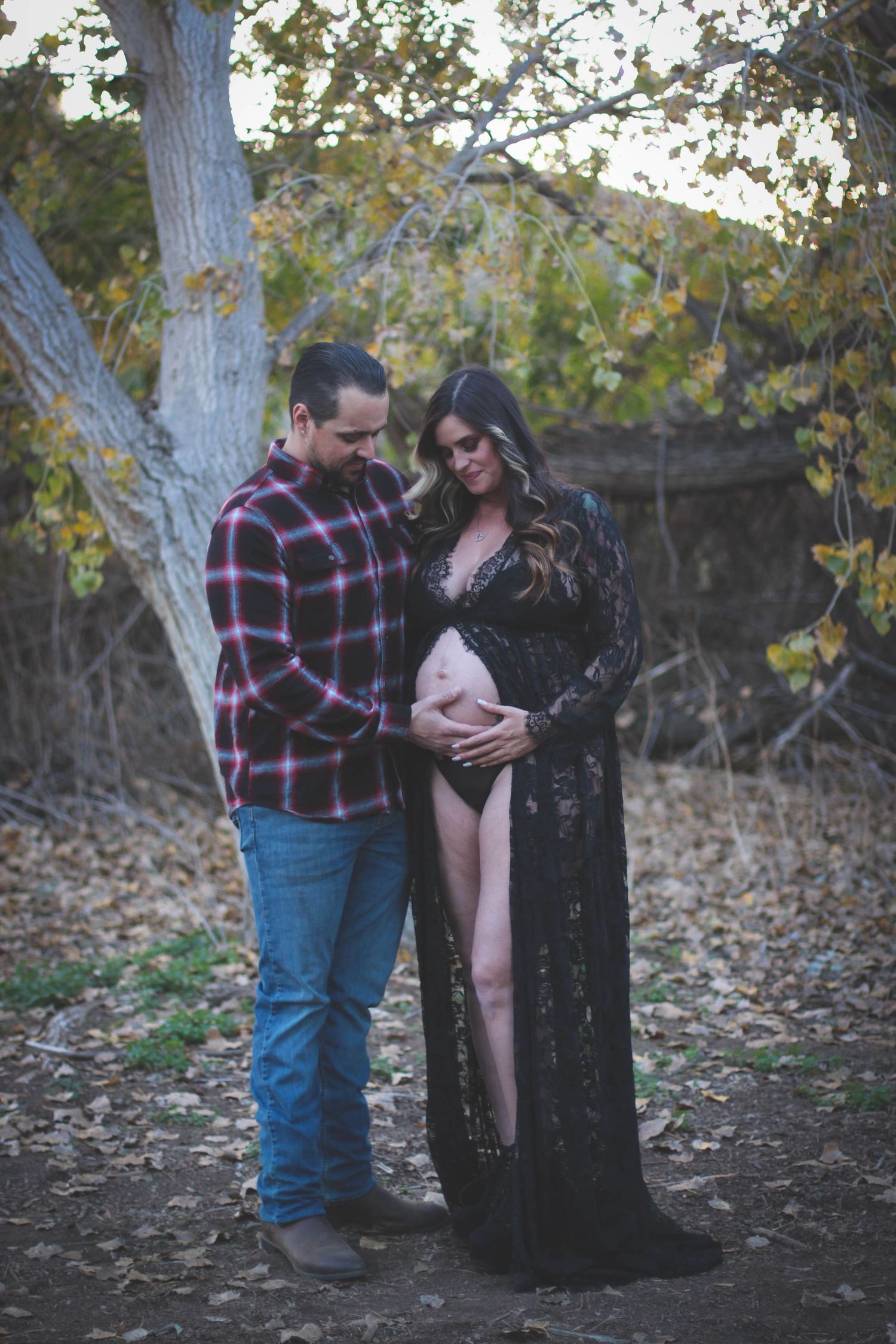 Couple sharing intimate moment during outdoor maternity photoshoot among autumn trees.