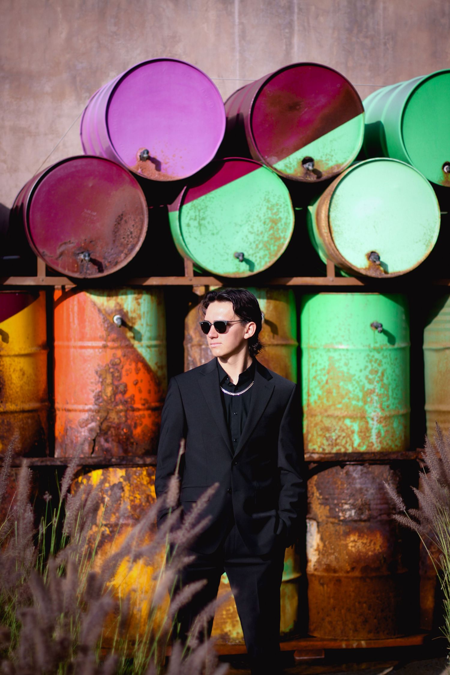 Artistic portrait with colorful industrial barrels creating dramatic backdrop.