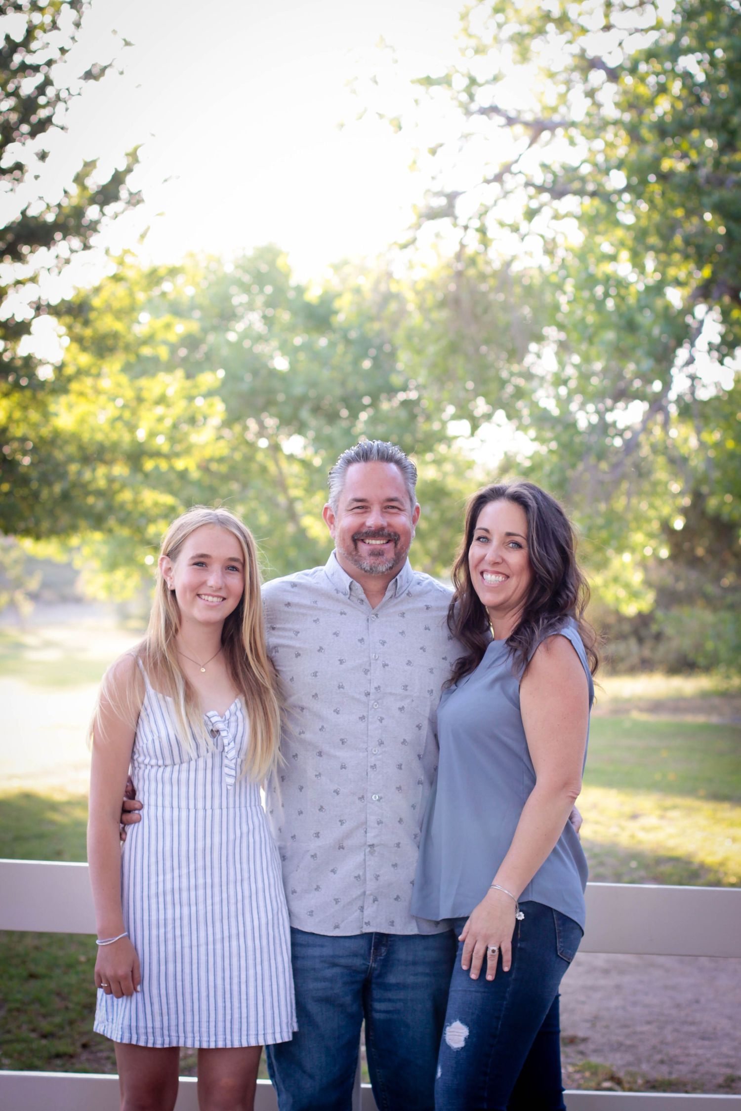 Family trio poses together outdoors in casual summer clothing.