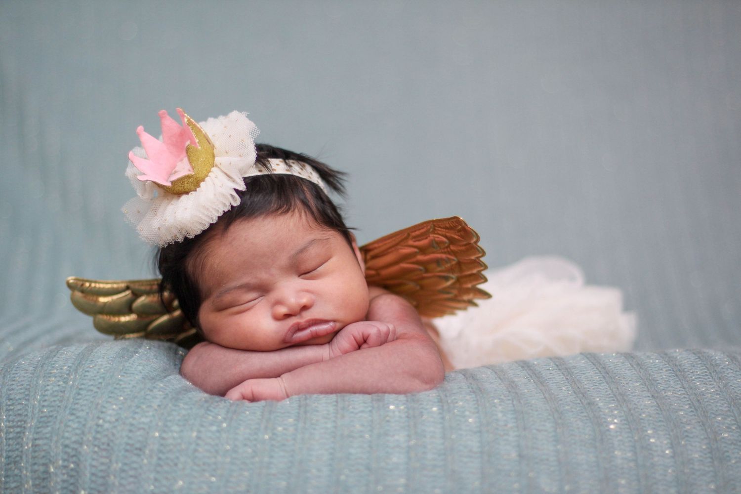 Sleeping newborn baby wrapped in soft white blankets against grey background.