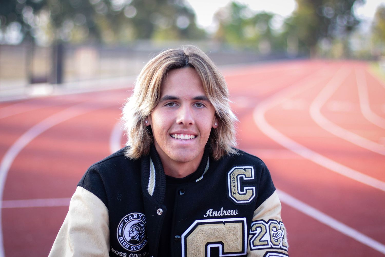 Senior photos on red running track wearing varsity letterman jacket.