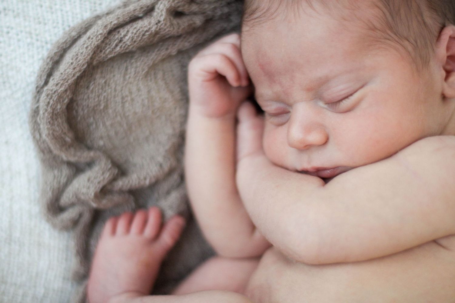 Peaceful newborn sleeping on white textured blanket in natural light.