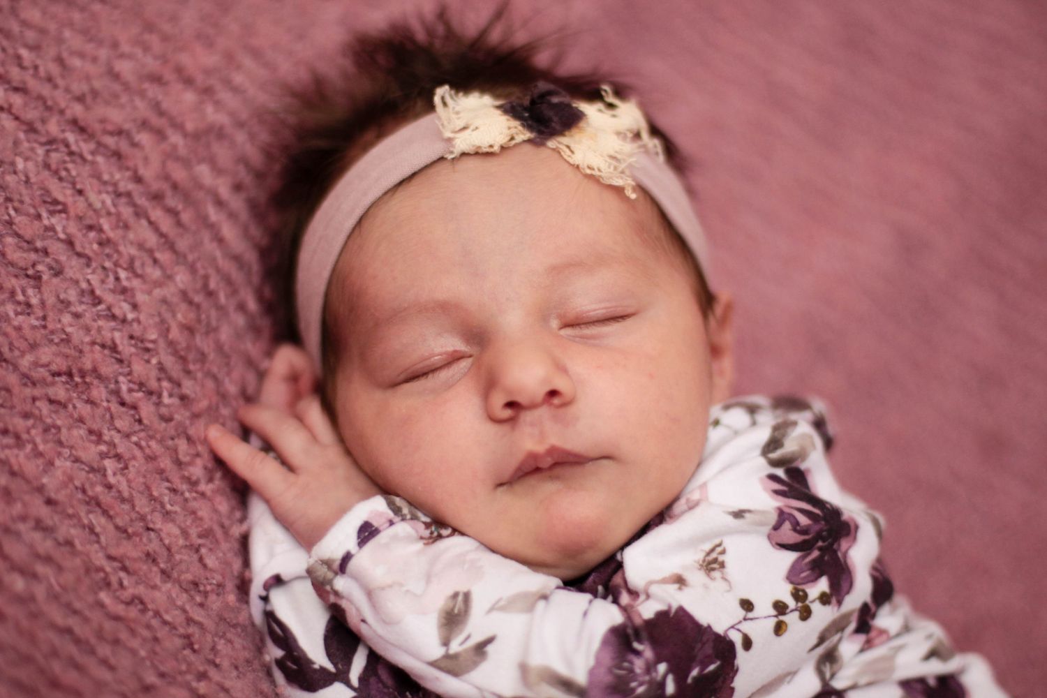 Baby sleeping peacefully on pink textured background with floral accessories.