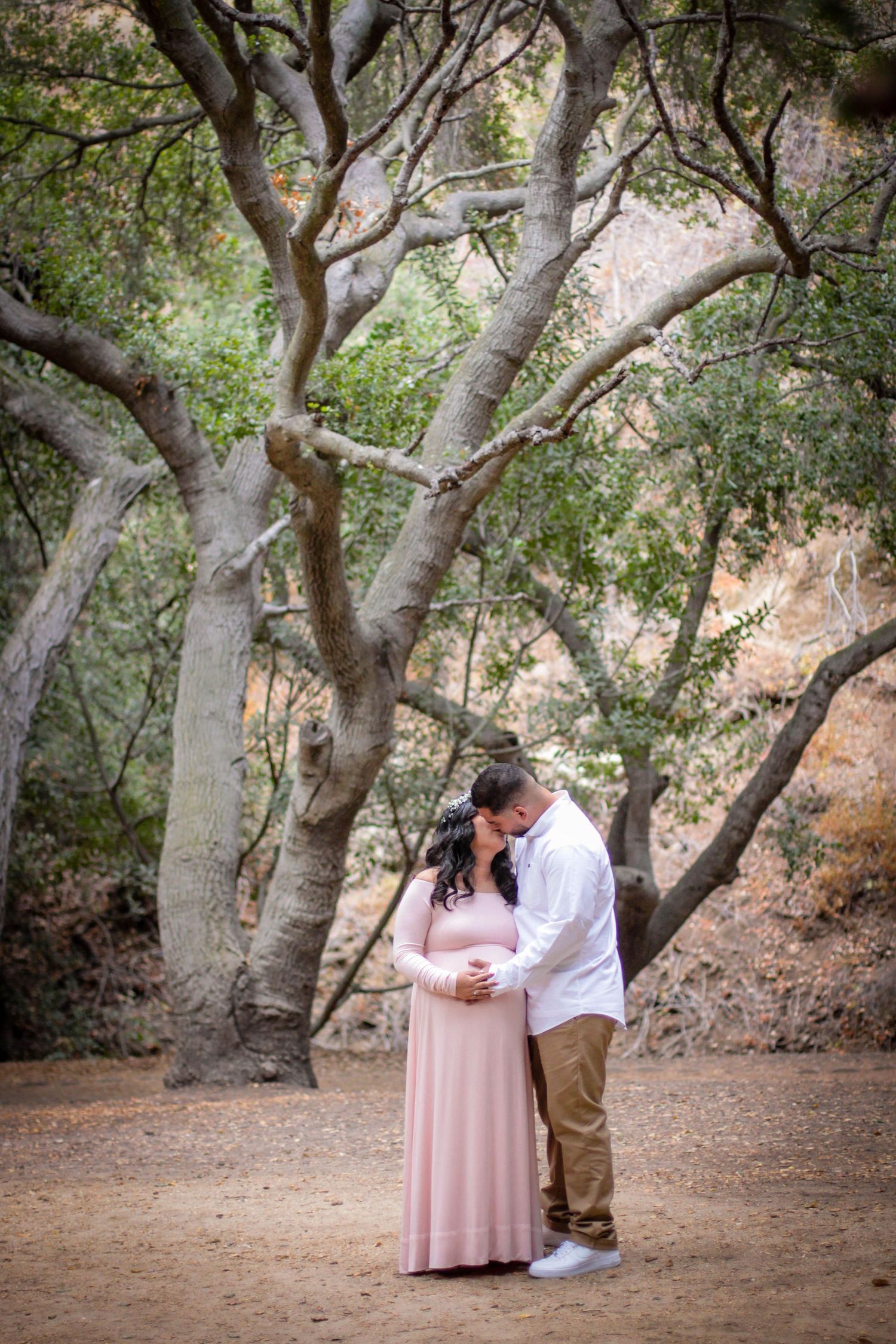 Romantic outdoor maternity photoshoot under a canopy of oak trees in natural lighting.