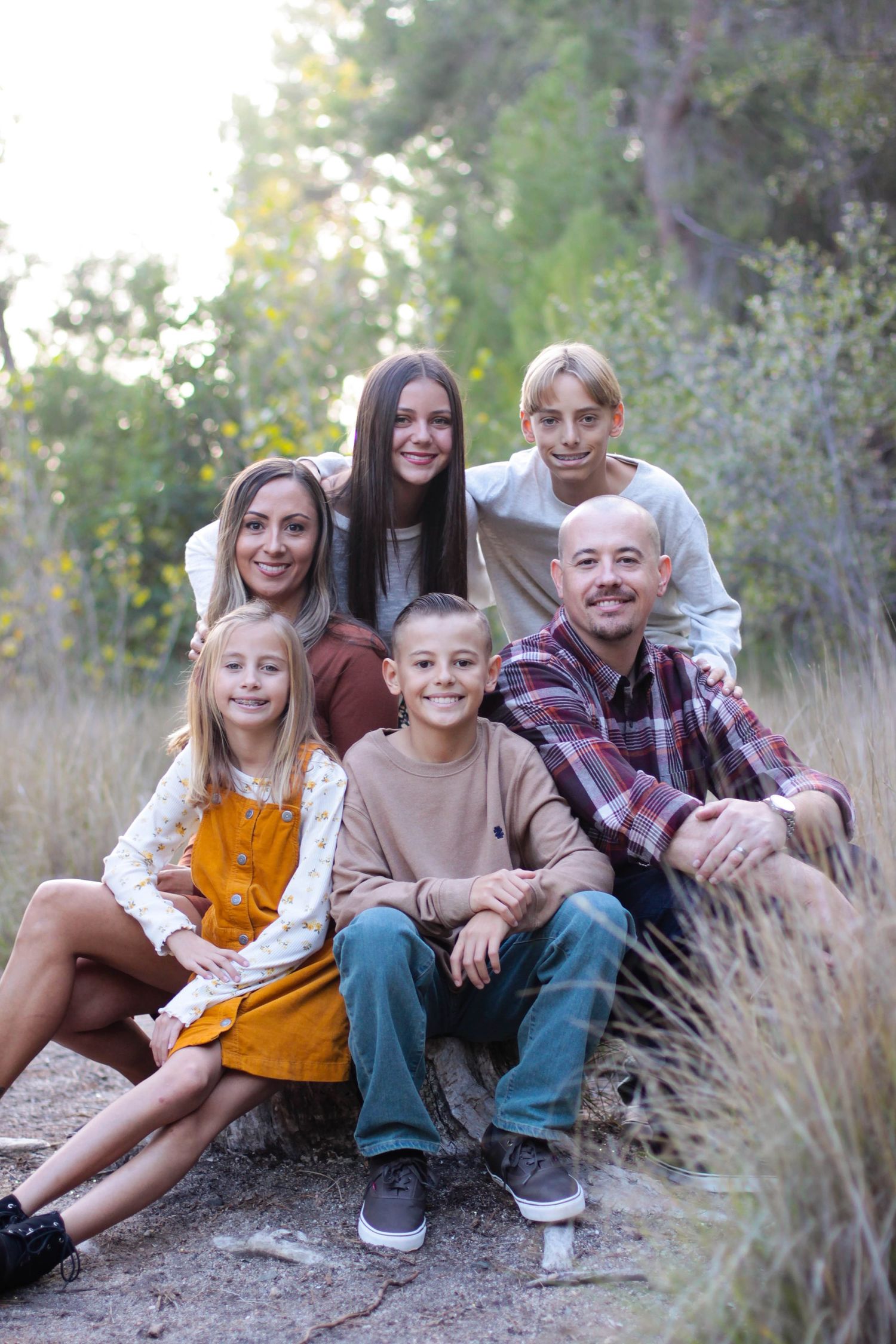 Family group sitting together on rocky ground surrounded by tall grass and trees.