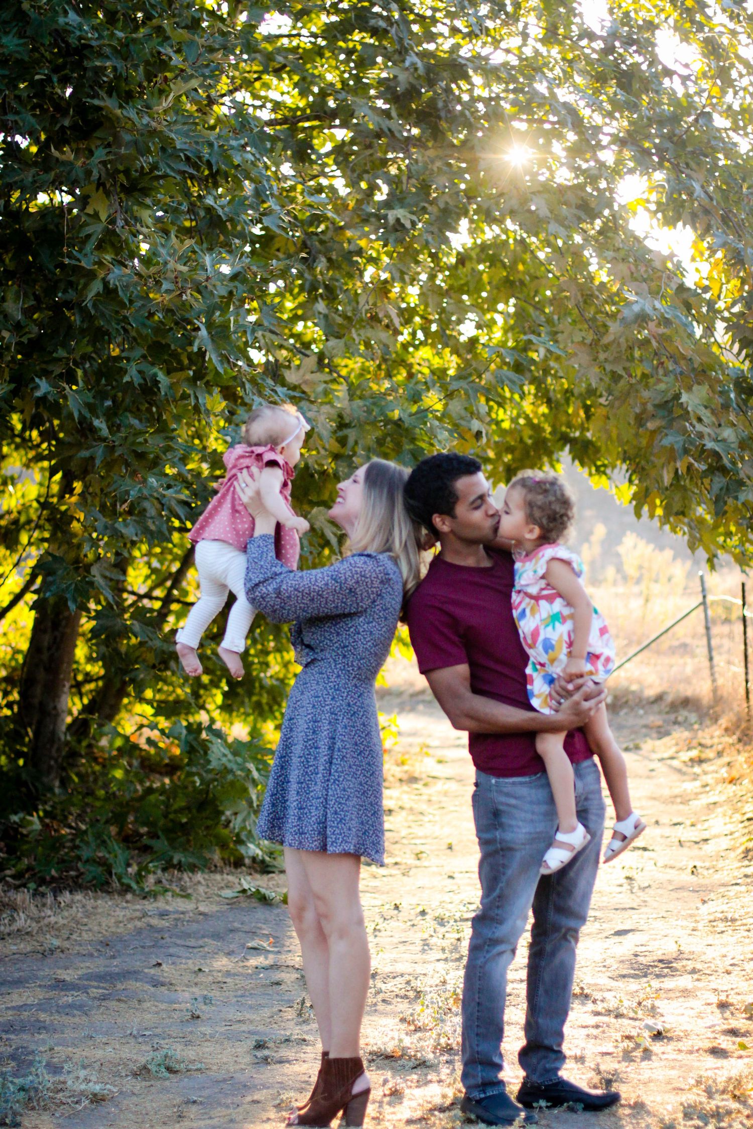 Family enjoying a playful moment together in a sunlit outdoor setting with trees in the background.
