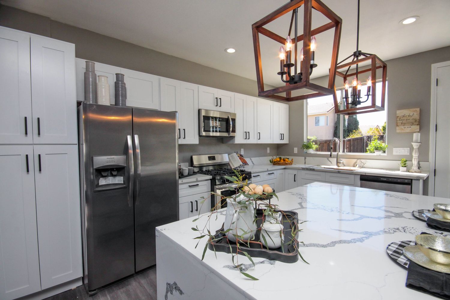Modern white kitchen with quartz countertops, stainless appliances and rustic pendant lighting.