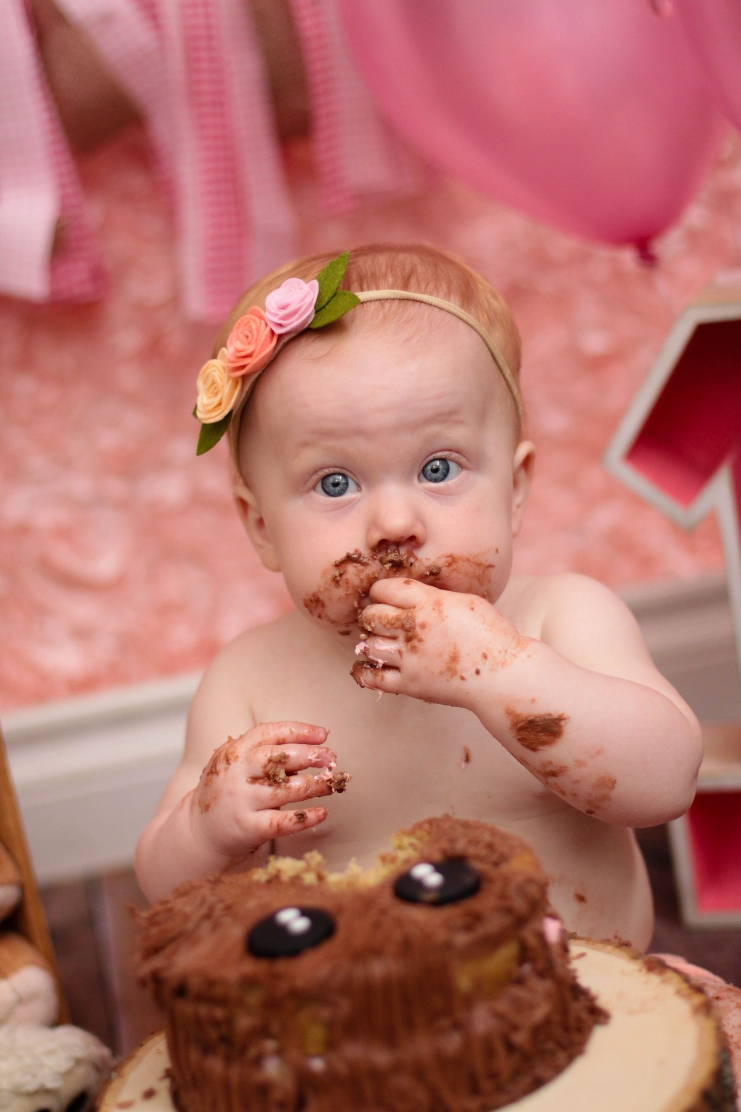 Baby enjoying first birthday cake smash with chocolate frosting all over.