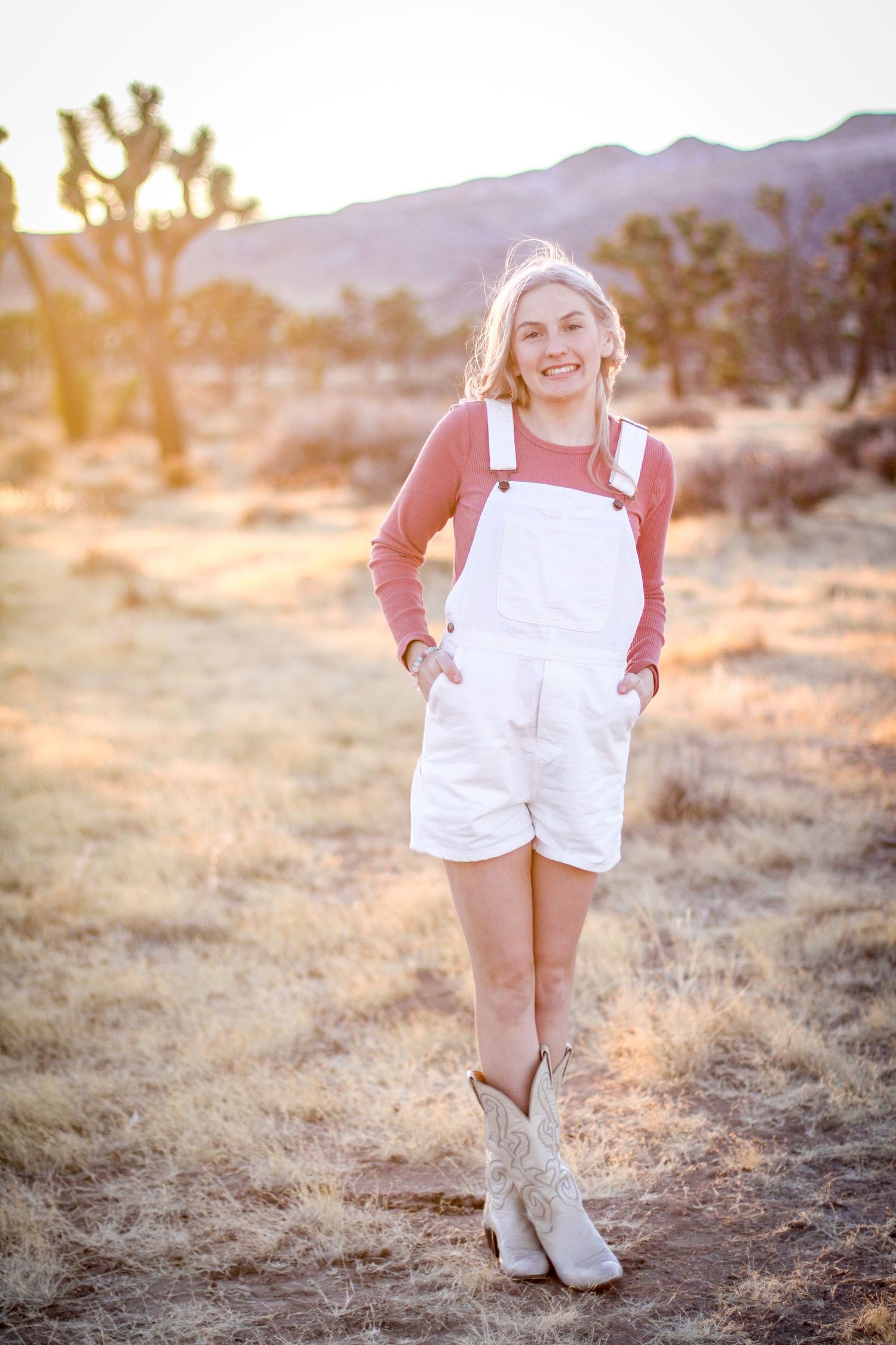 Child in white overalls running through desert landscape at sunset.