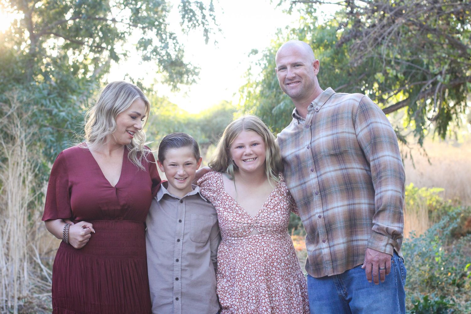 Group portrait of a family dressed in burgundy and neutral tones against a natural outdoor backdrop.