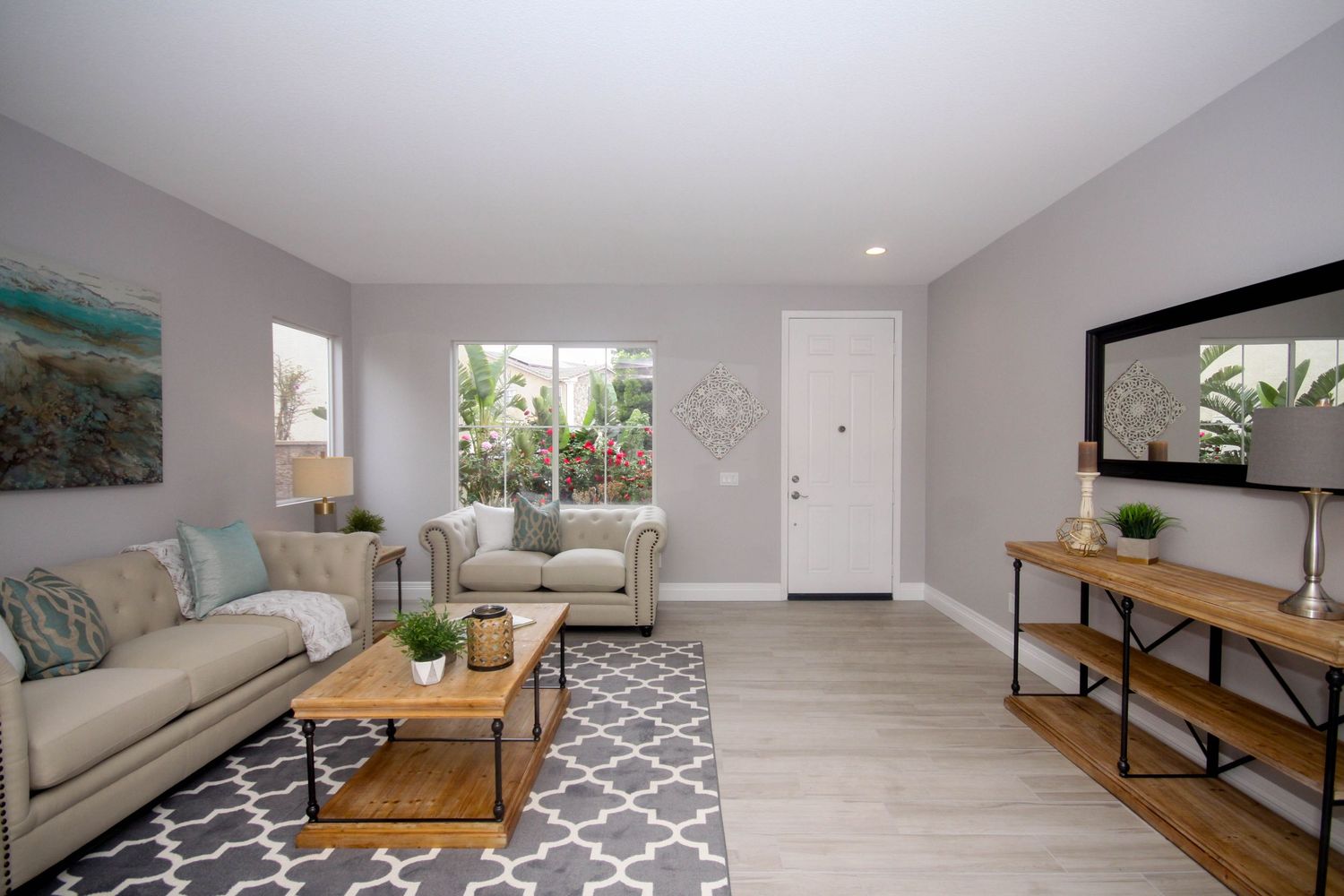 Modern living room with gray walls, patterned area rug, beige sofa and wooden accent furniture.