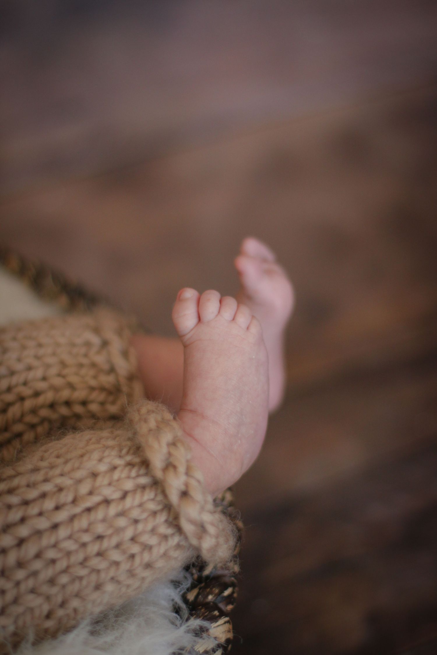 Close-up of tiny baby feet wrapped in knitted beige blanket.