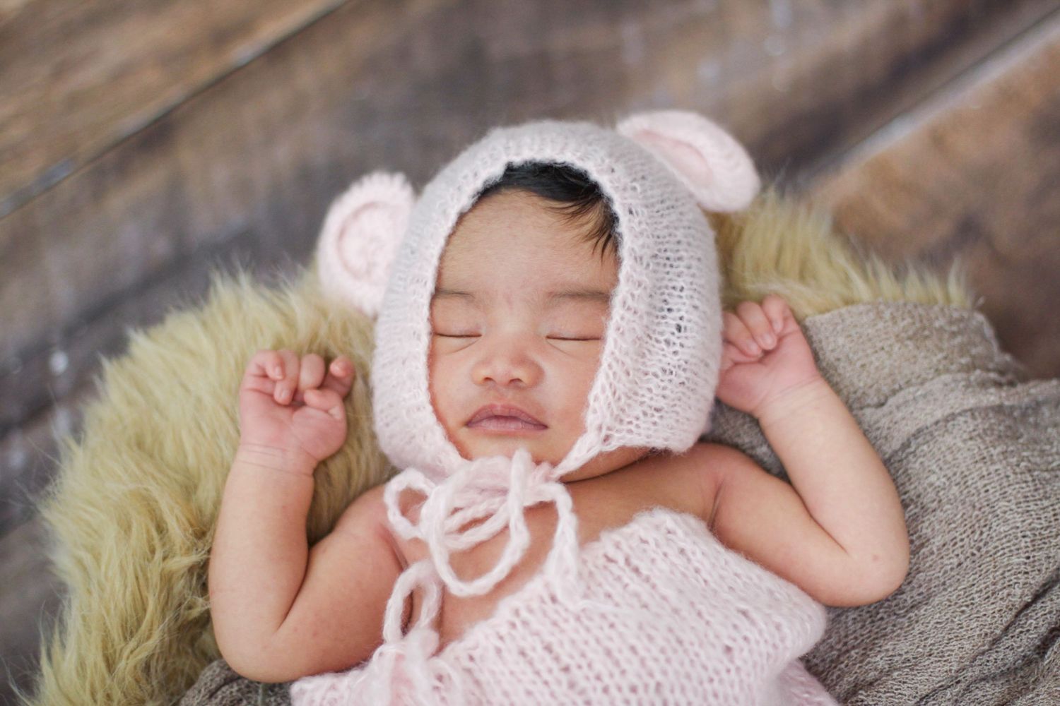 Peaceful newborn baby wearing pink bonnet resting on plush fabric.