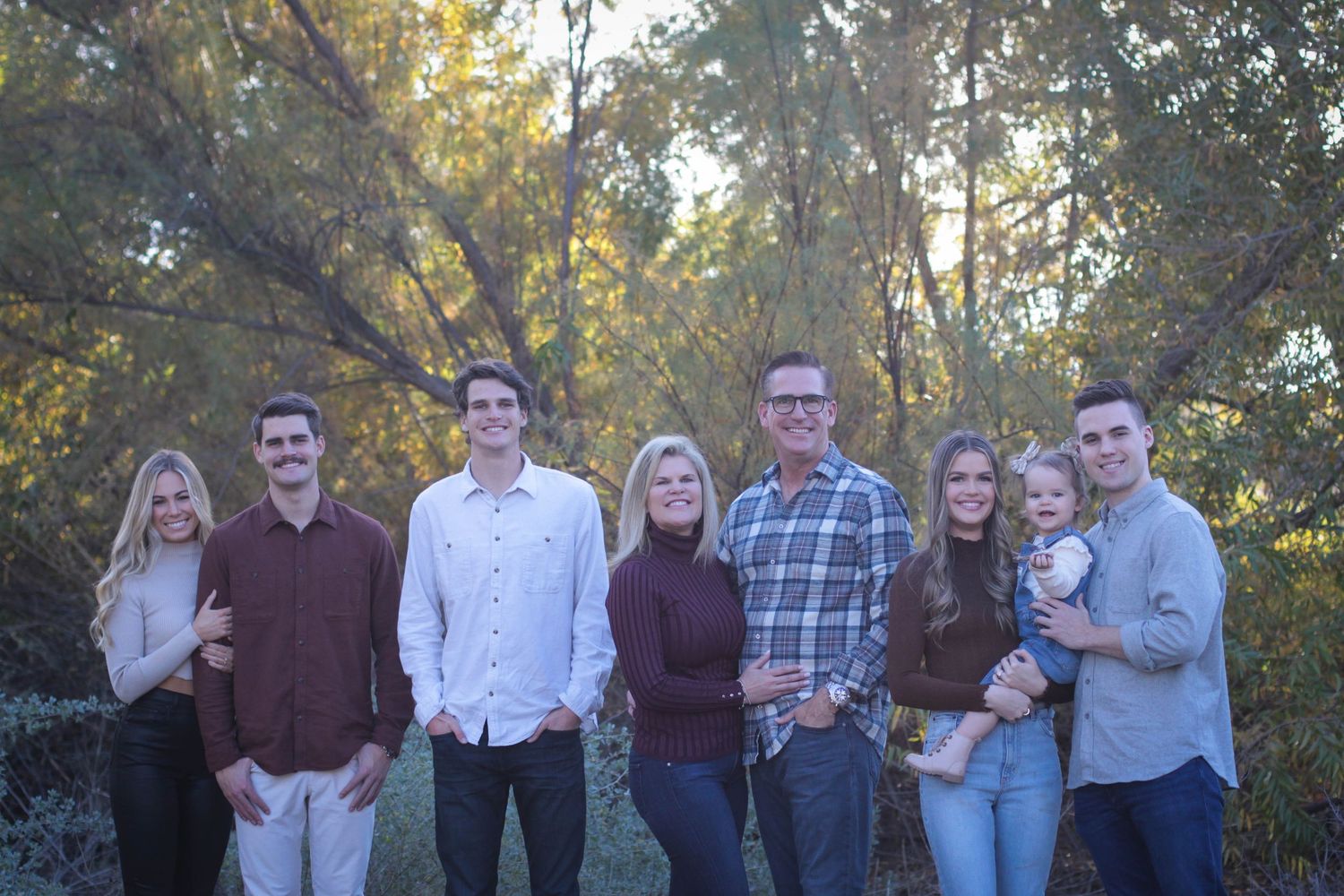 Extended family group poses together in natural outdoor setting during sunset.