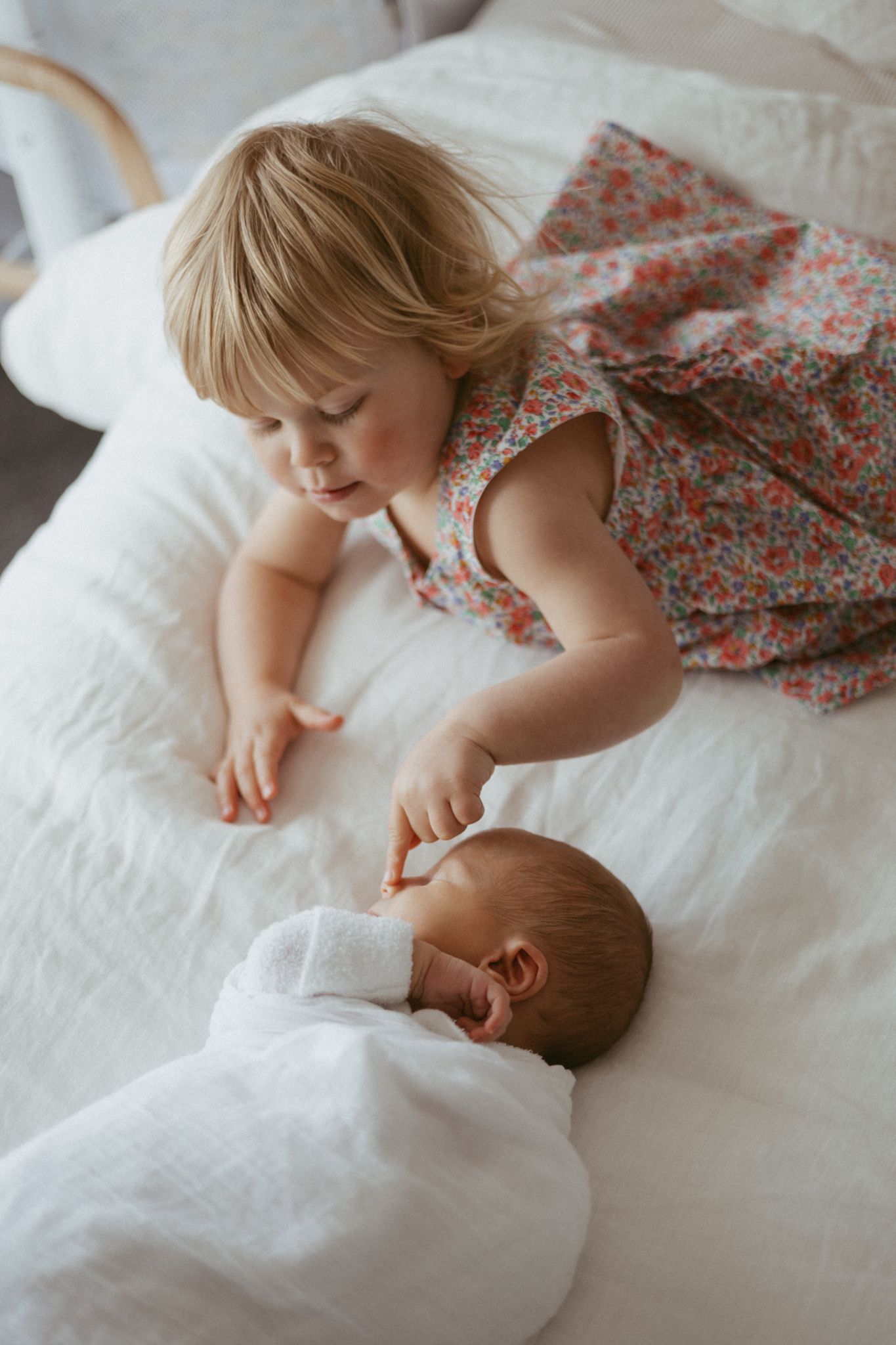 A series of tender moments showing a young child and baby interacting on white bedding with floral patterns. newborn photoshoot. lifestyle