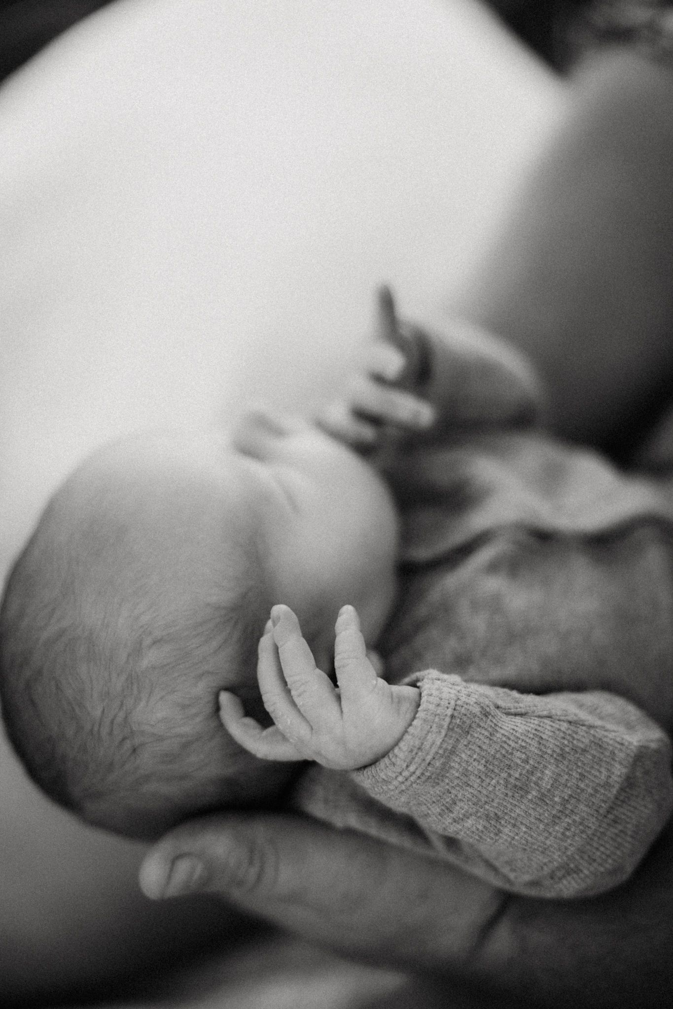 Black and white photo of a newborn baby being cradled, showing tiny delicate fingers and peaceful sleeping pose.