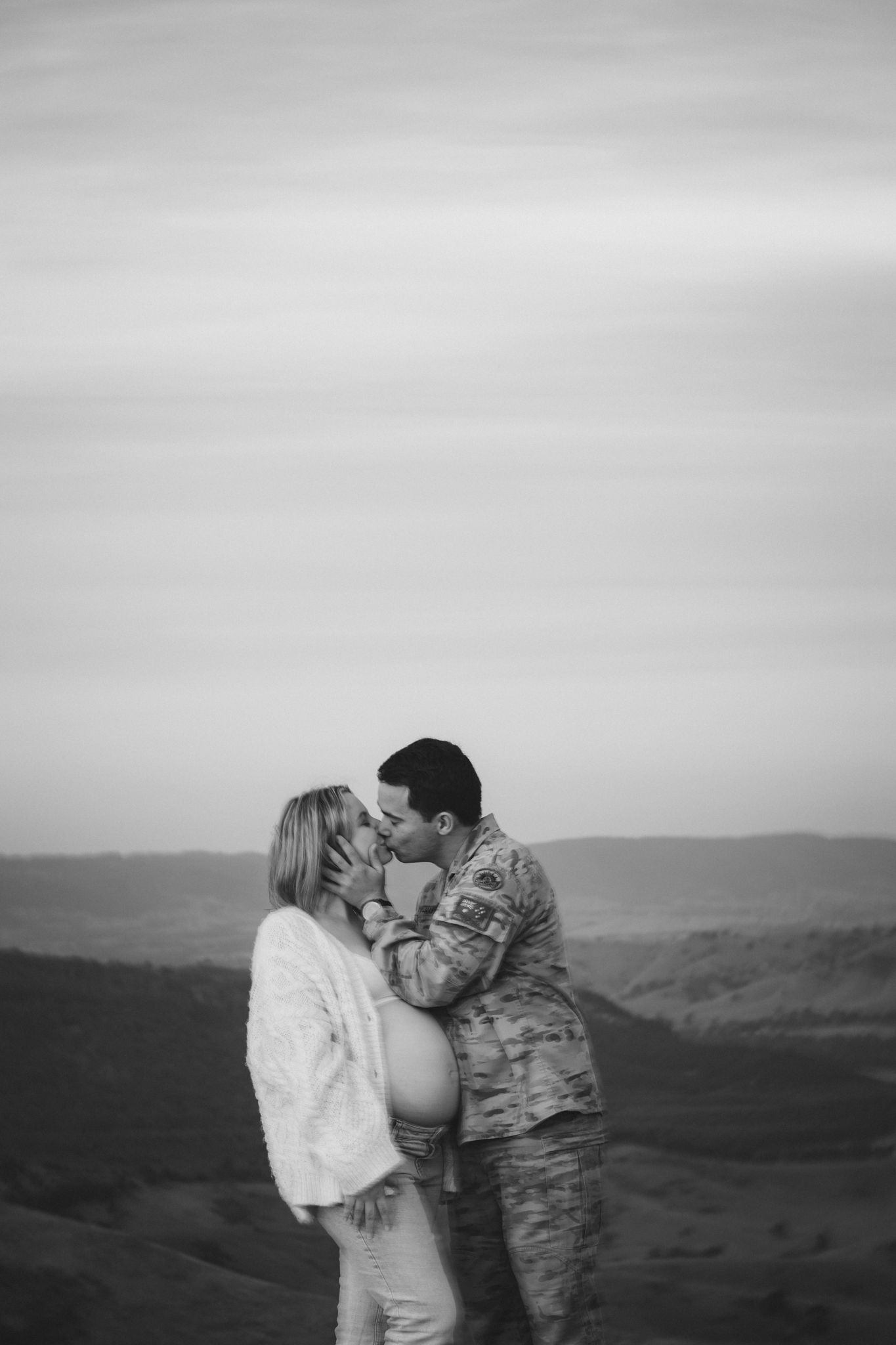 A couple shares an intimate moment against a scenic mountain backdrop in black and white. hilltop views