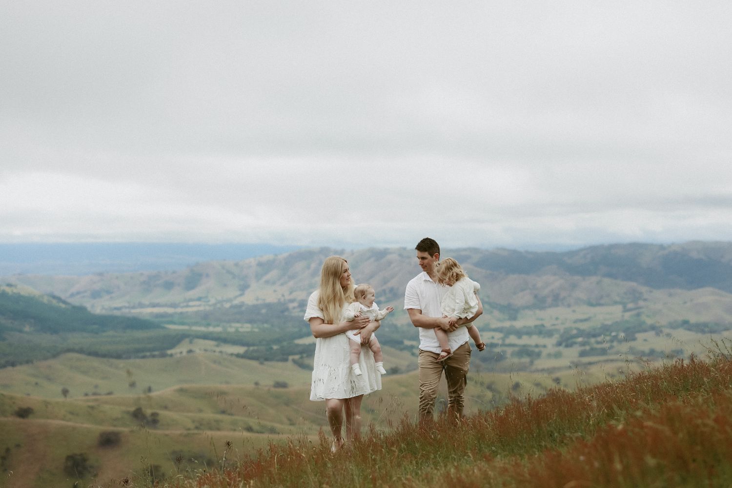 Family of four standing on a scenic hilltop with rolling green valleys and mountains in the background.
