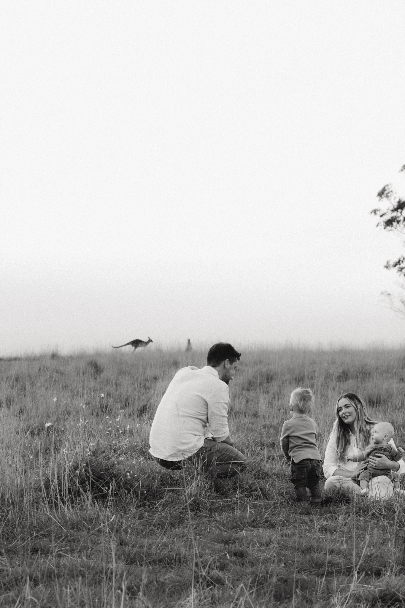Black and white photo of a family with two young children sitting together in a grassy field on a misty day.