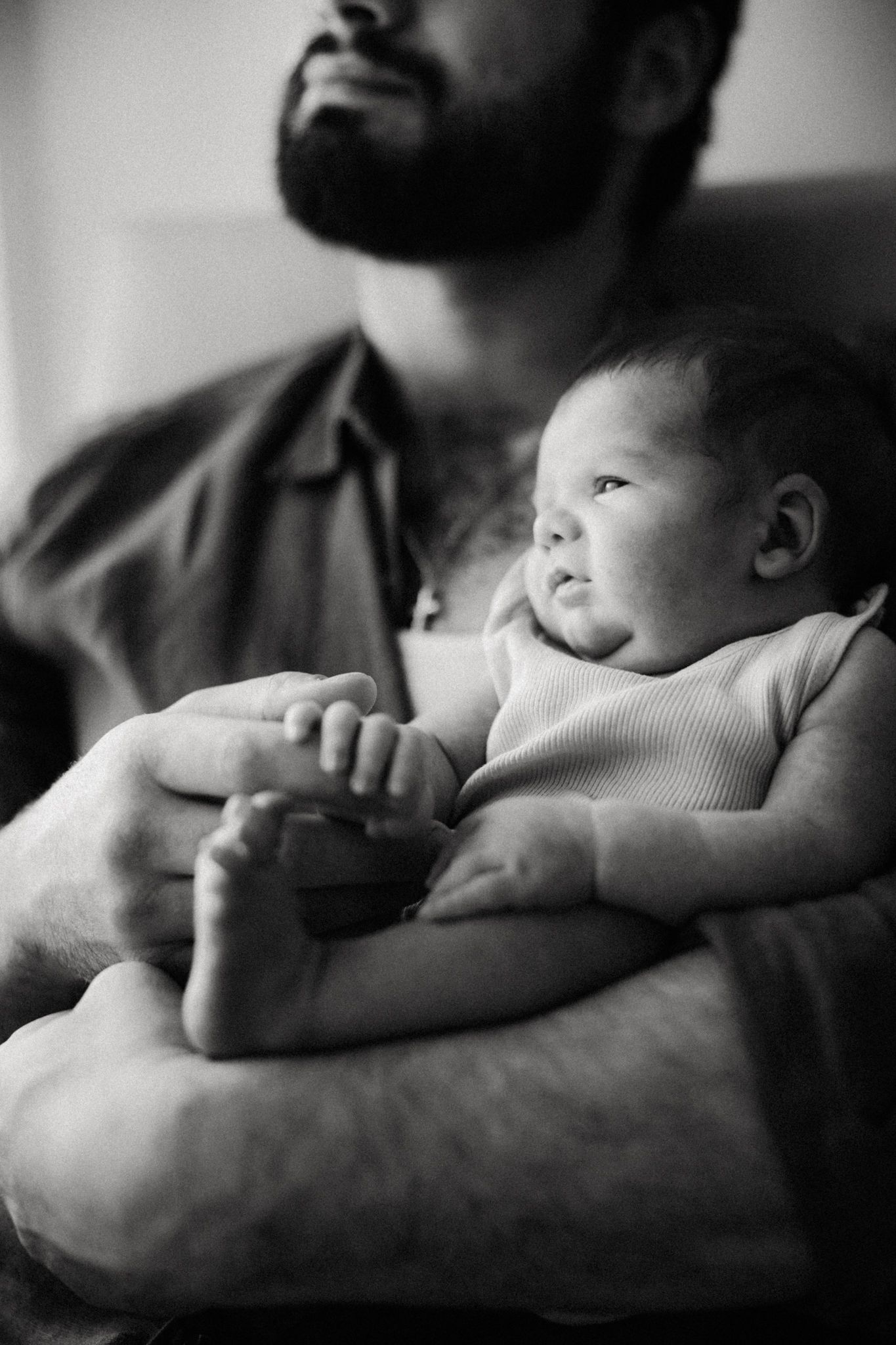 Black and white photo of a bearded father cradling his newborn baby in his arms.
