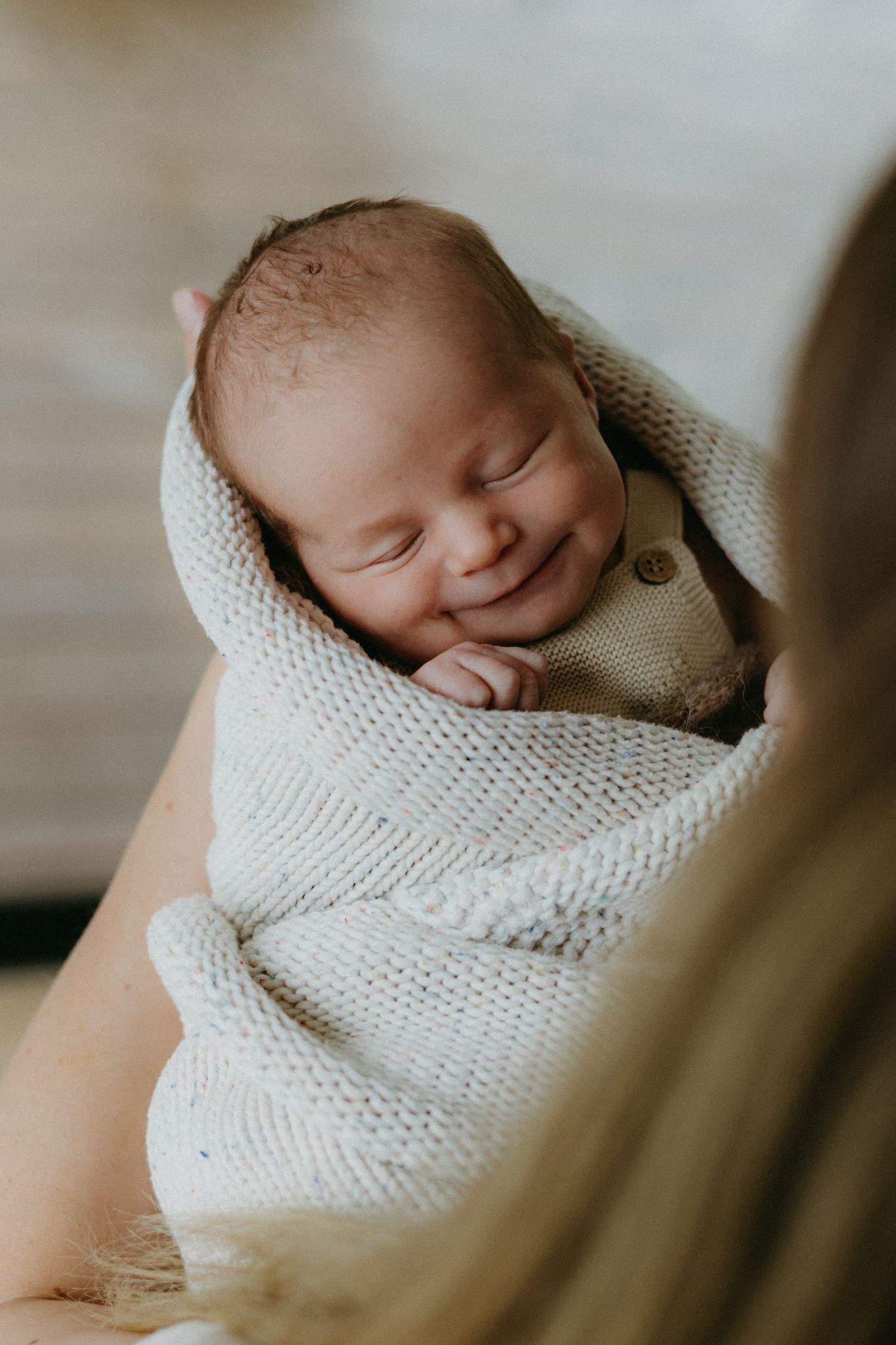 Smiling newborn baby wrapped in a soft knit blanket being cradled in mother's arms.
